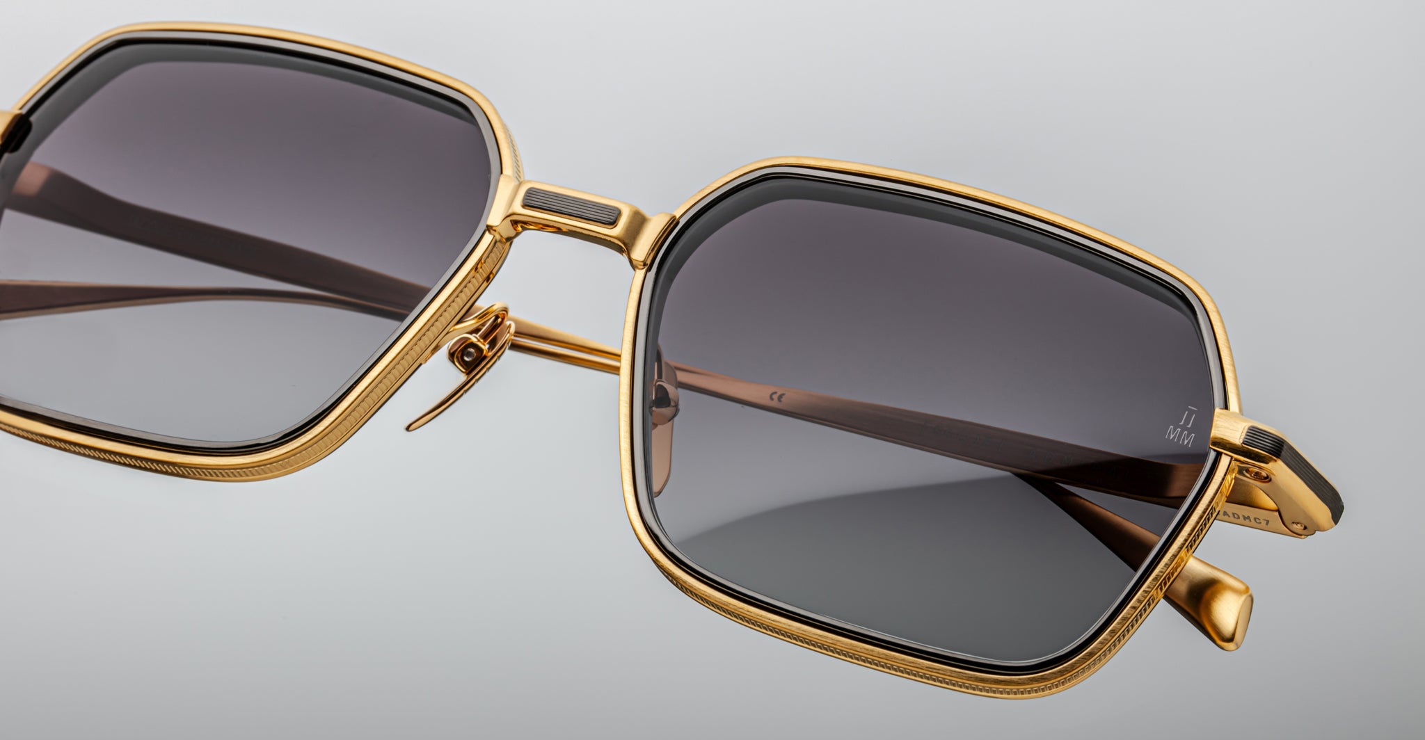 Close-up of Jacques Marie Mage Admiral sunglasses, featuring gold square frames and dark lenses, photographed from the front.