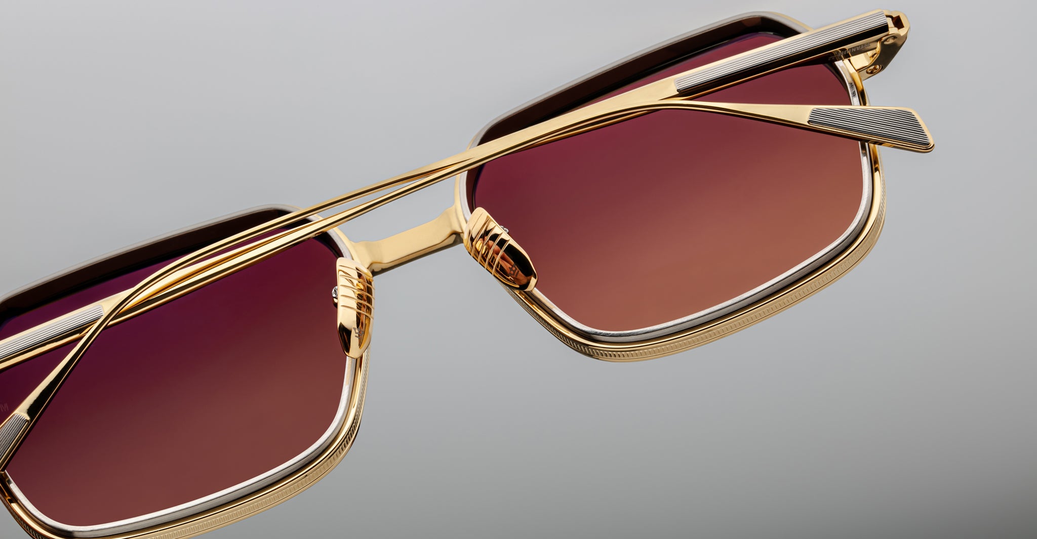 Close-up of Jacques Marie Mage Admiral sunglasses featuring gold square frames, red lenses, and slim metal arms.