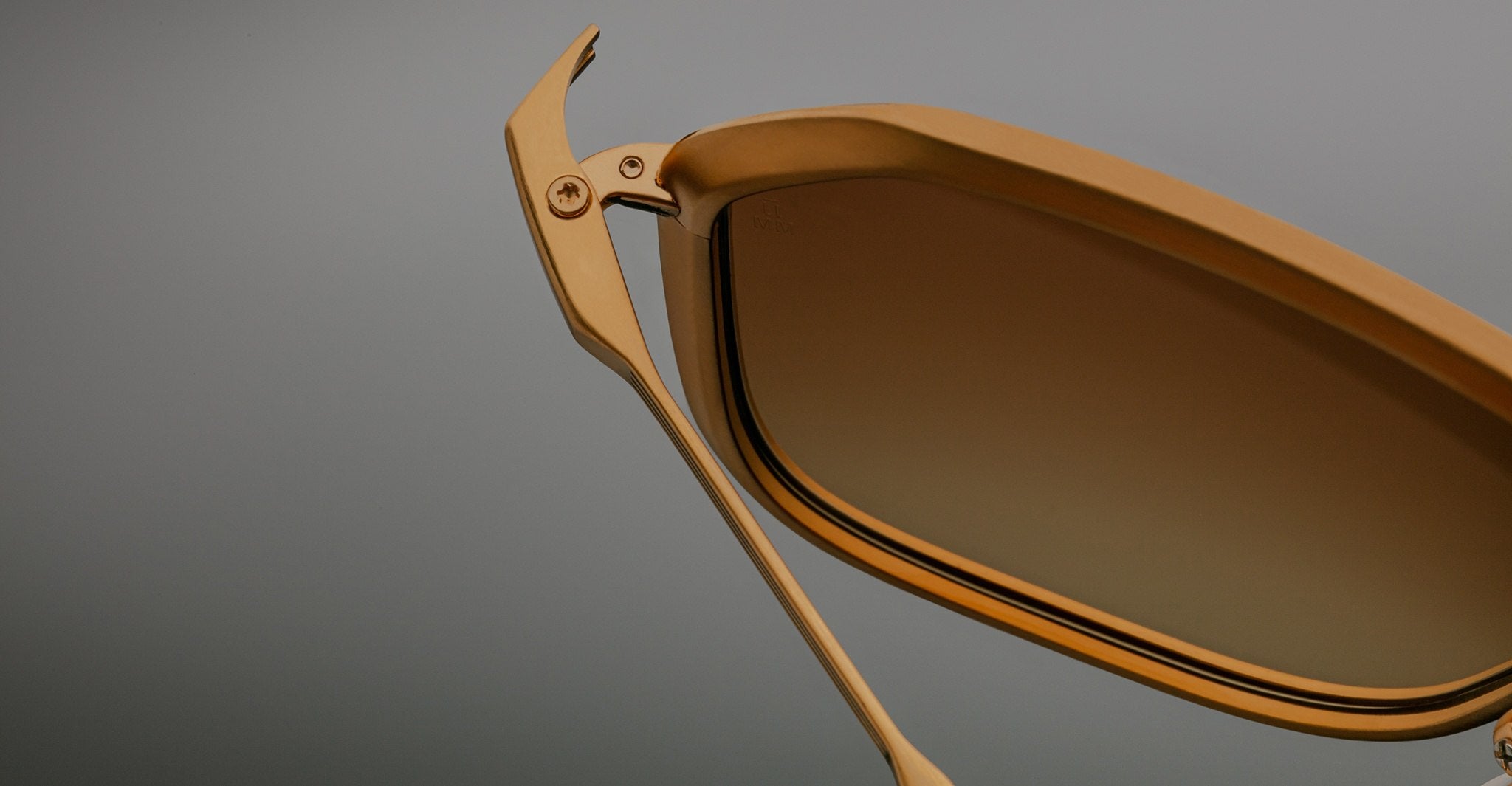 Close-up of Jacques Marie Mage Aida sunglasses in gold-tone metal, highlighting the faceted rim, hinge detail, and brown gradient lens.