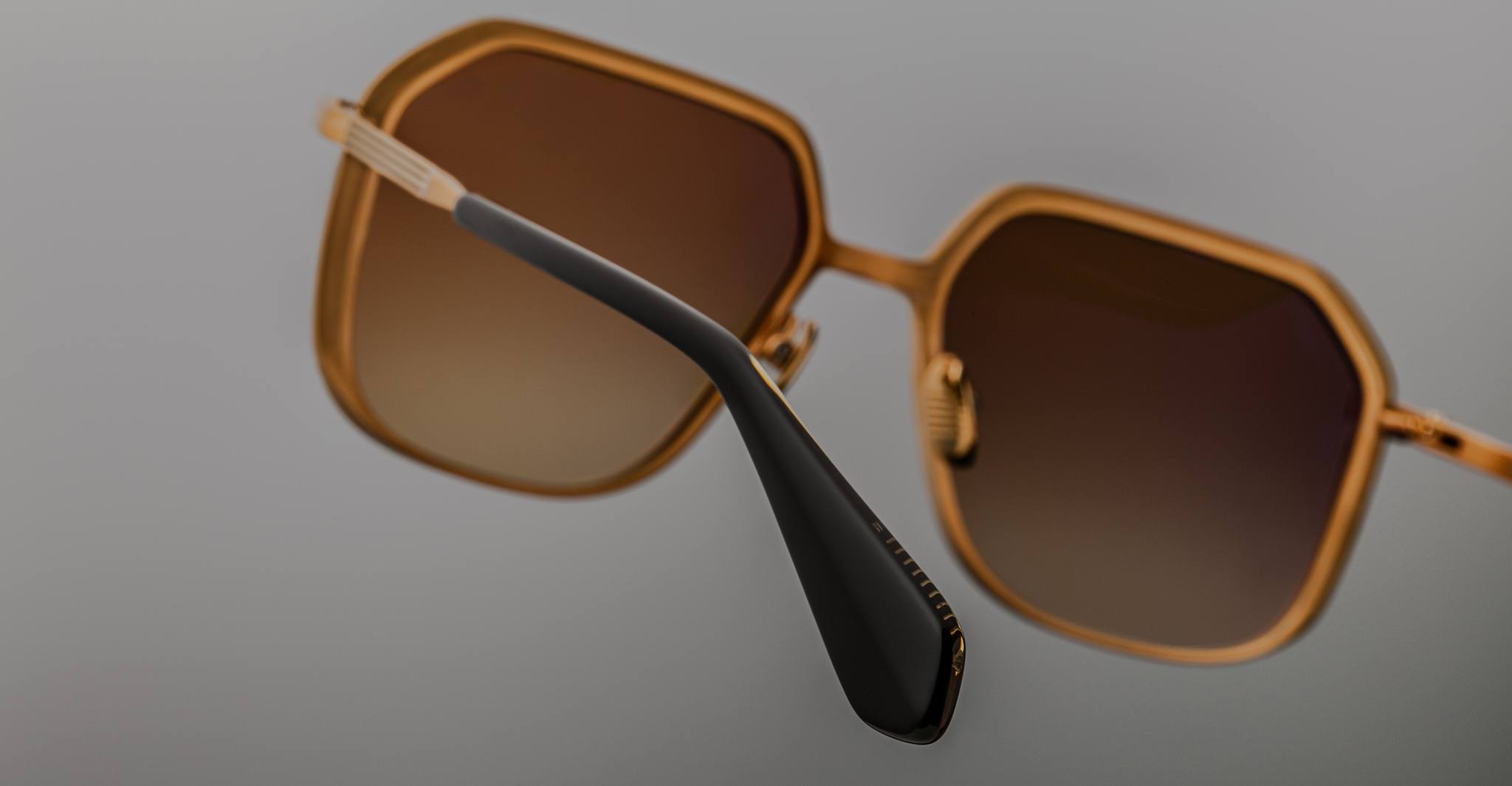 Angled view of Jacques Marie Mage Aida sunglasses in gold-tone metal, featuring geometric lenses with brown gradient tint and a black acetate temple tip.