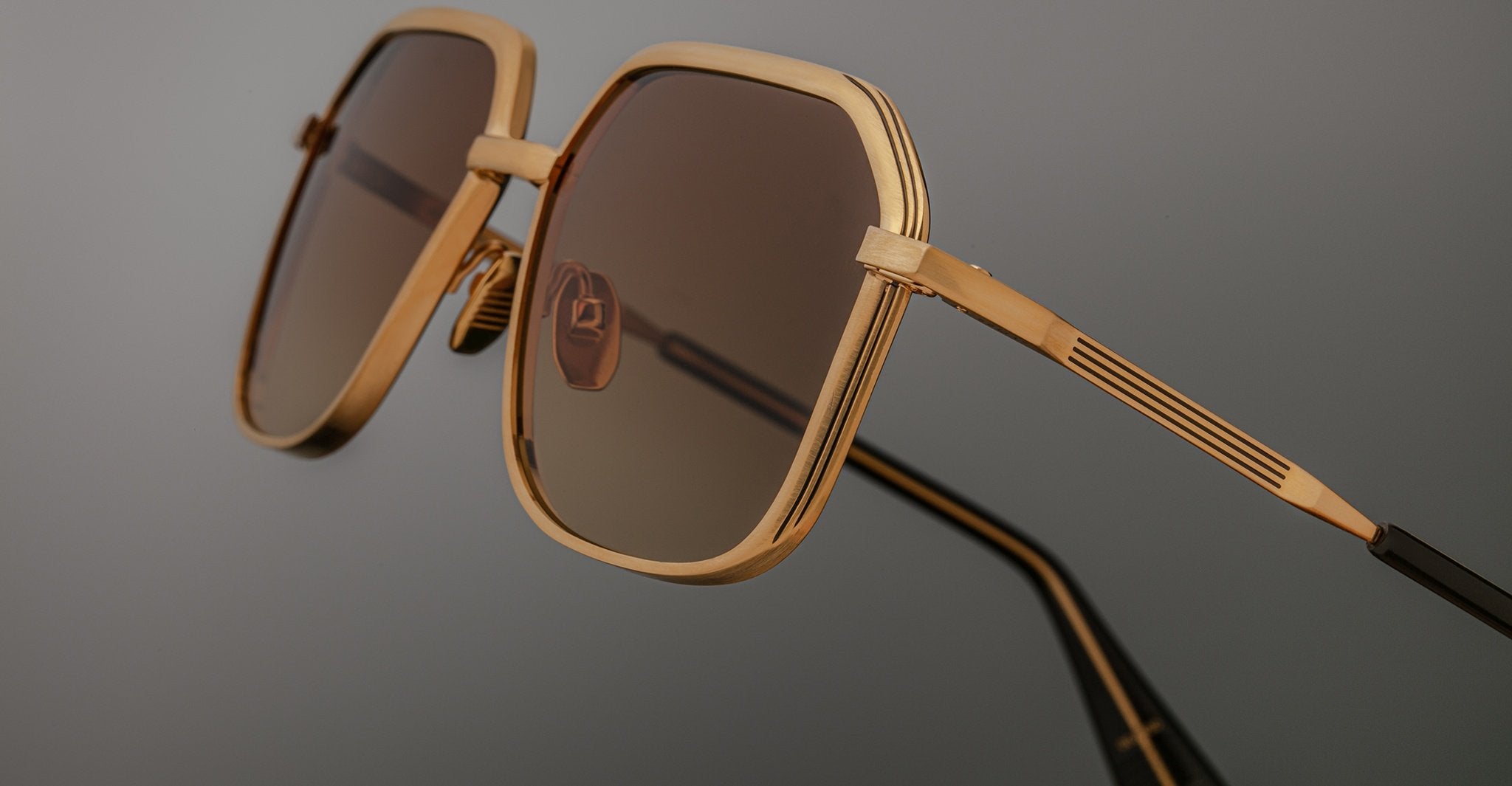 Angled side view of Jacques Marie Mage Aida sunglasses in gold-tone metal, highlighting the faceted geometric rim, engraved temple detail, adjustable nose pads, and brown gradient lenses.