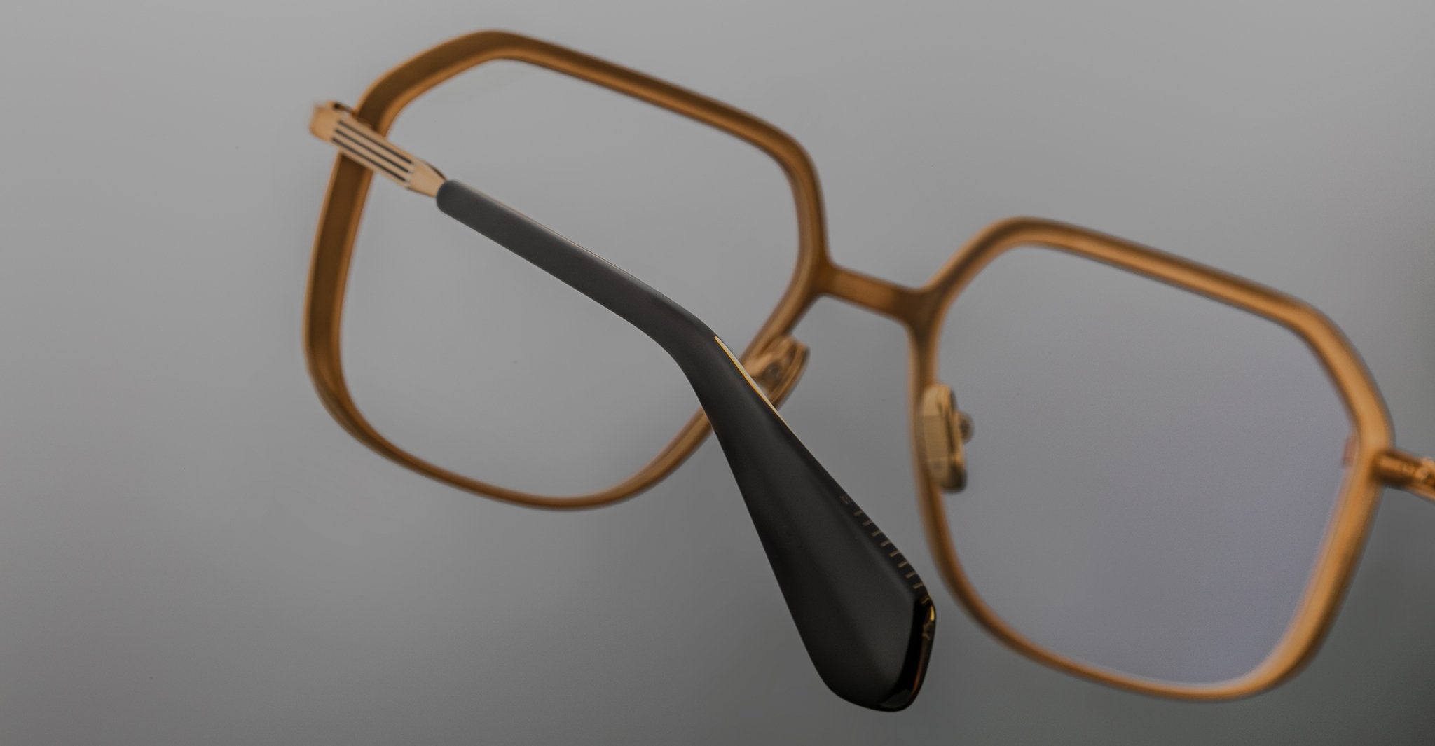 Angled view of Jacques Marie Mage Aida eyeglasses in gold-tone metal, showcasing the geometric square lens shape, sculpted bridge, and black acetate temple tip.