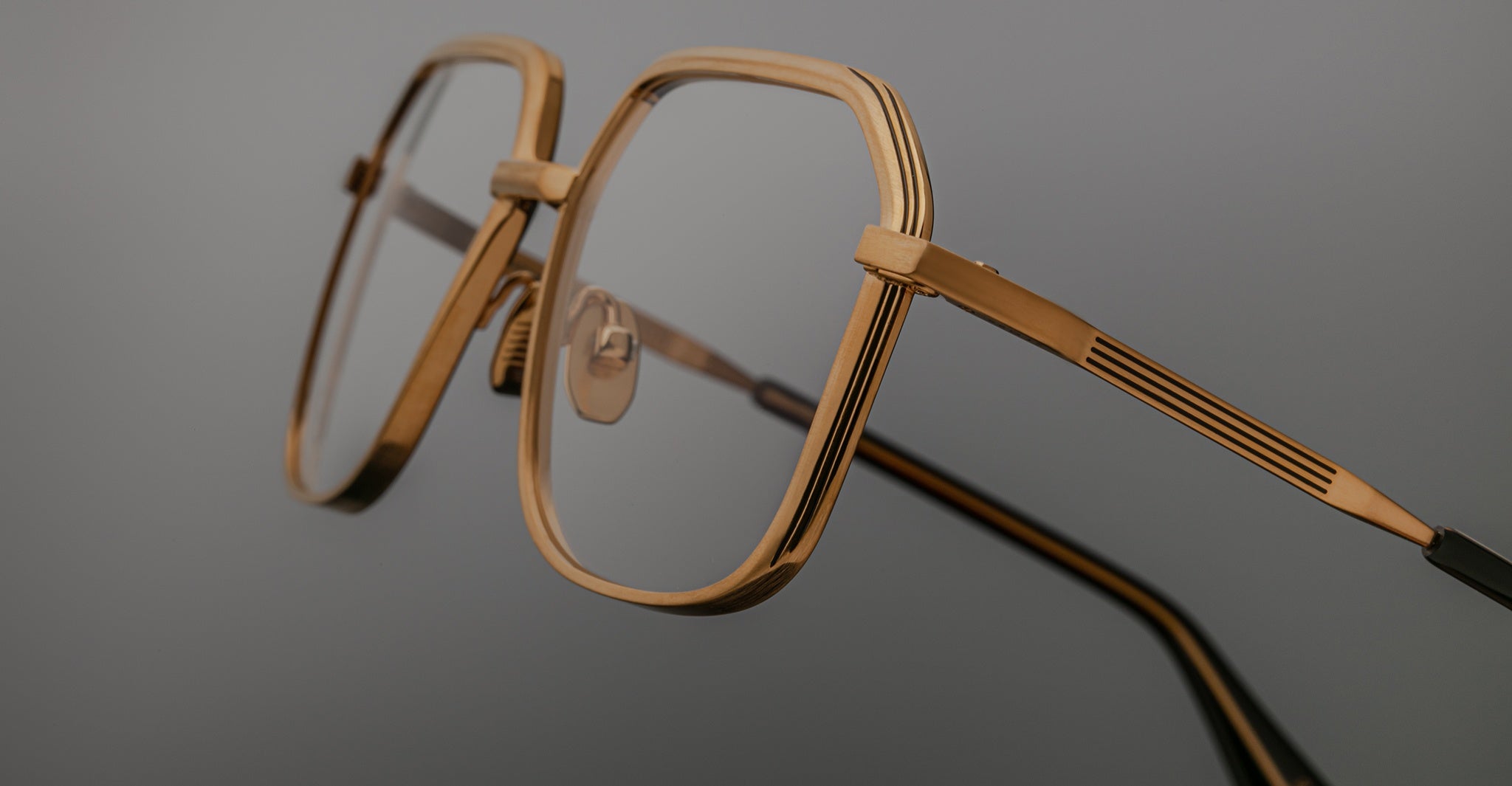 Angled side view of Jacques Marie Mage Aida eyeglasses in gold-tone metal, highlighting the faceted geometric rim, hinge construction, engraved temple detail, and adjustable nose pads.
