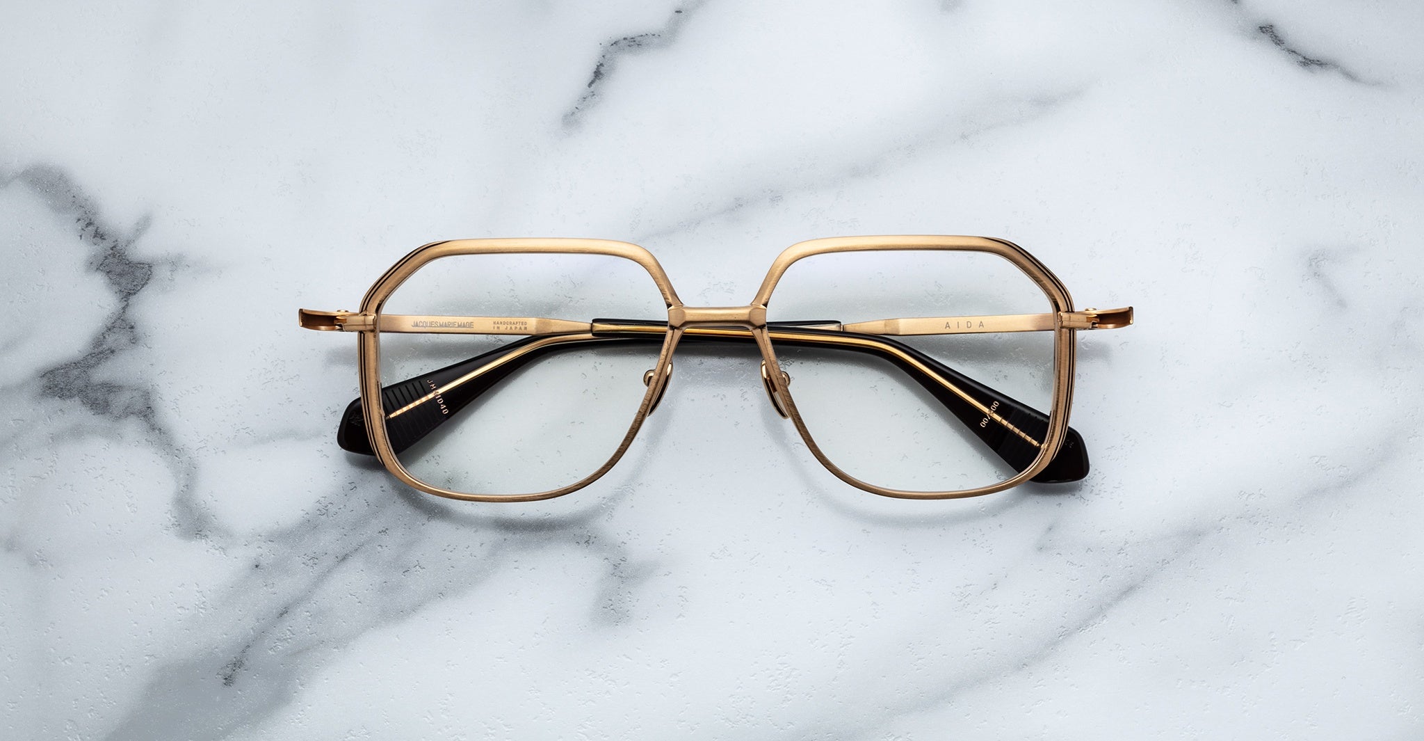 Jacques Marie Mage Aida eyeglasses in gold-tone metal, featuring a geometric square aviator shape with a double bridge and black temple tips, front view on a neutral background.