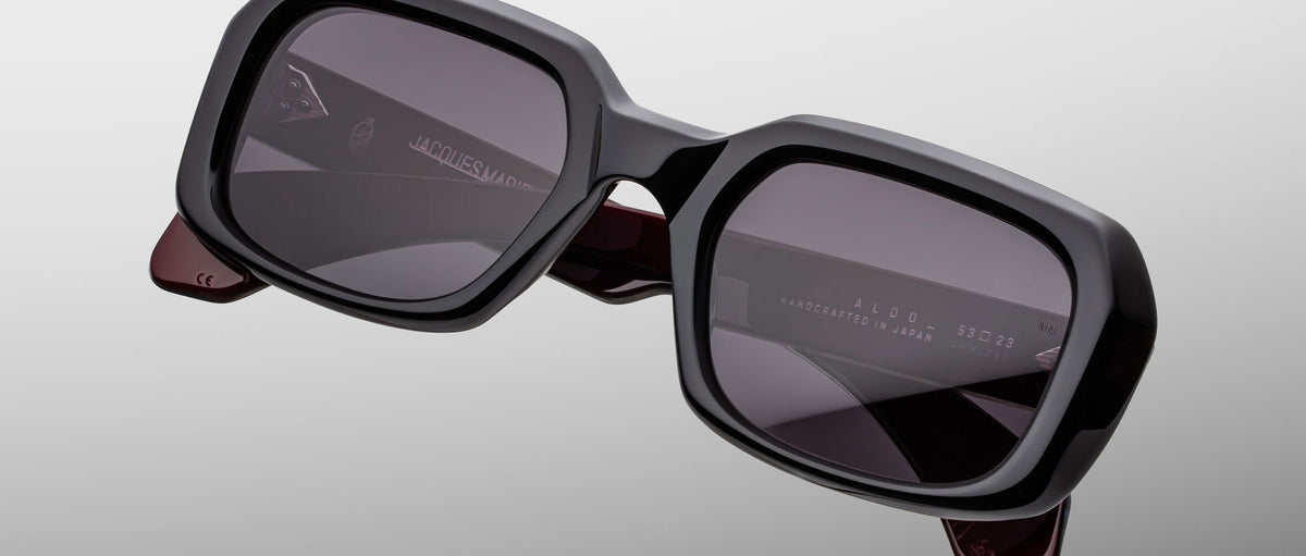 Jacques Marie Mage Aldo sunglasses, bold black square frames with dark lenses and maroon inner arms, front angle view.