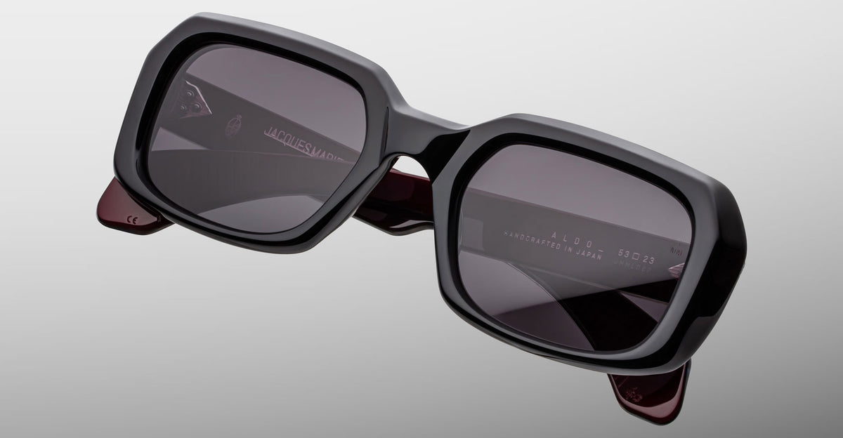 Jacques Marie Mage Aldo sunglasses, bold black square frames with dark lenses and maroon inner arms, front angle view.