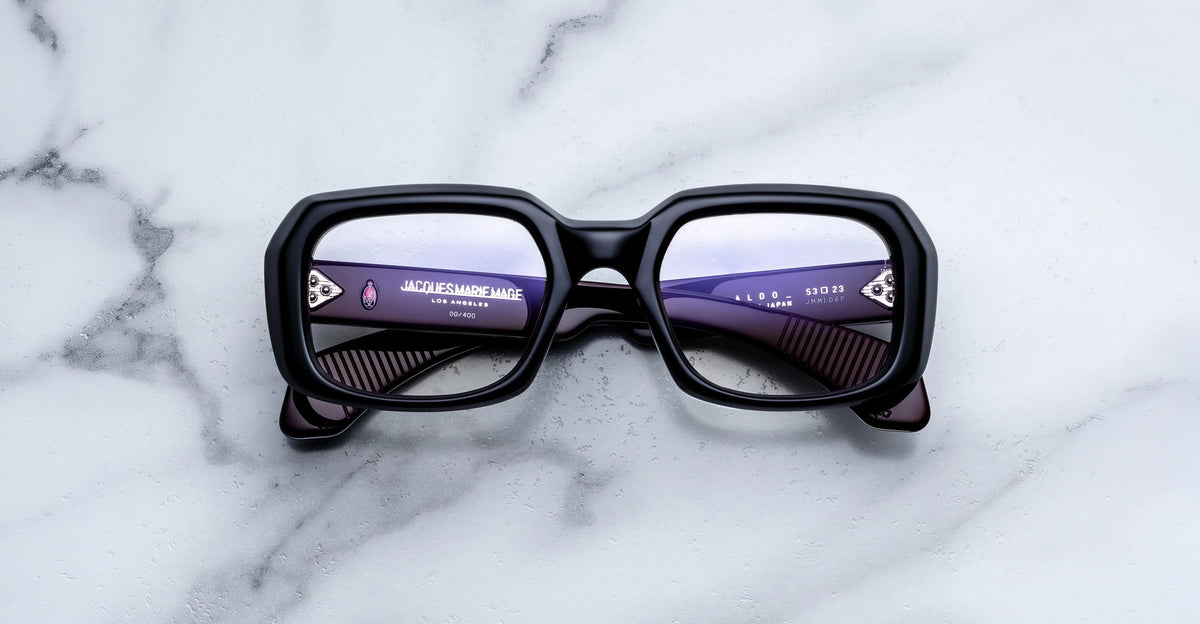 Jacques Marie Mage Aldo black rectangular eyeglasses with digital text reflected in lenses, shown from above.