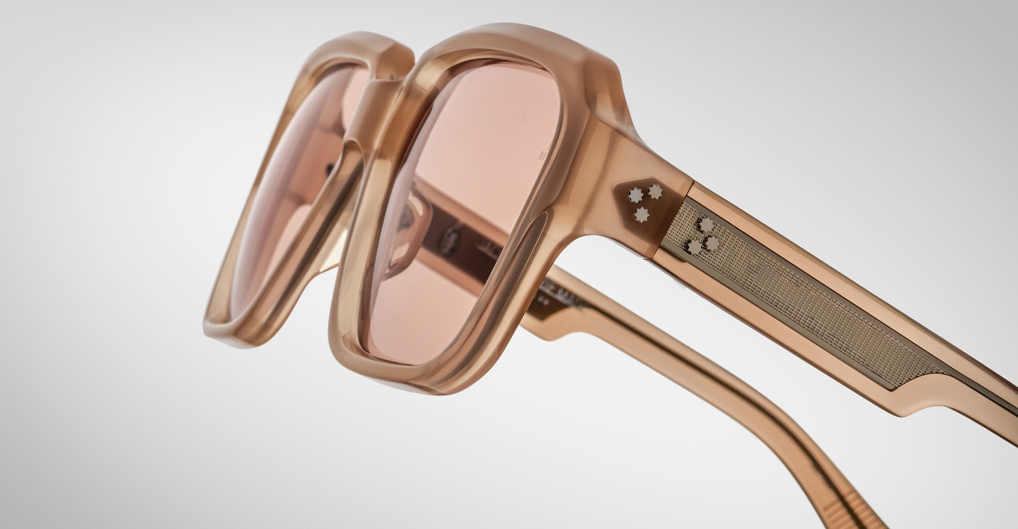 Close-up of Jacques Marie Mage Alfred oversized, square sunglasses in translucent peach with tinted lenses and textured temple arms, displayed on a plain white background.