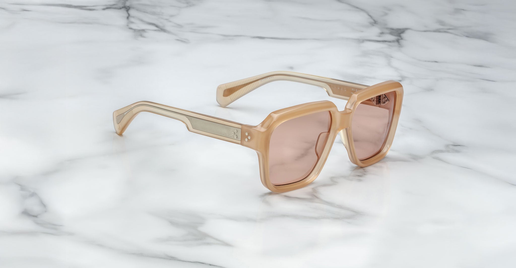 A pair of Jacques Marie Mage Alfred rectangular sunglasses with beige frames and light brown tinted lenses rests on a white marble surface.