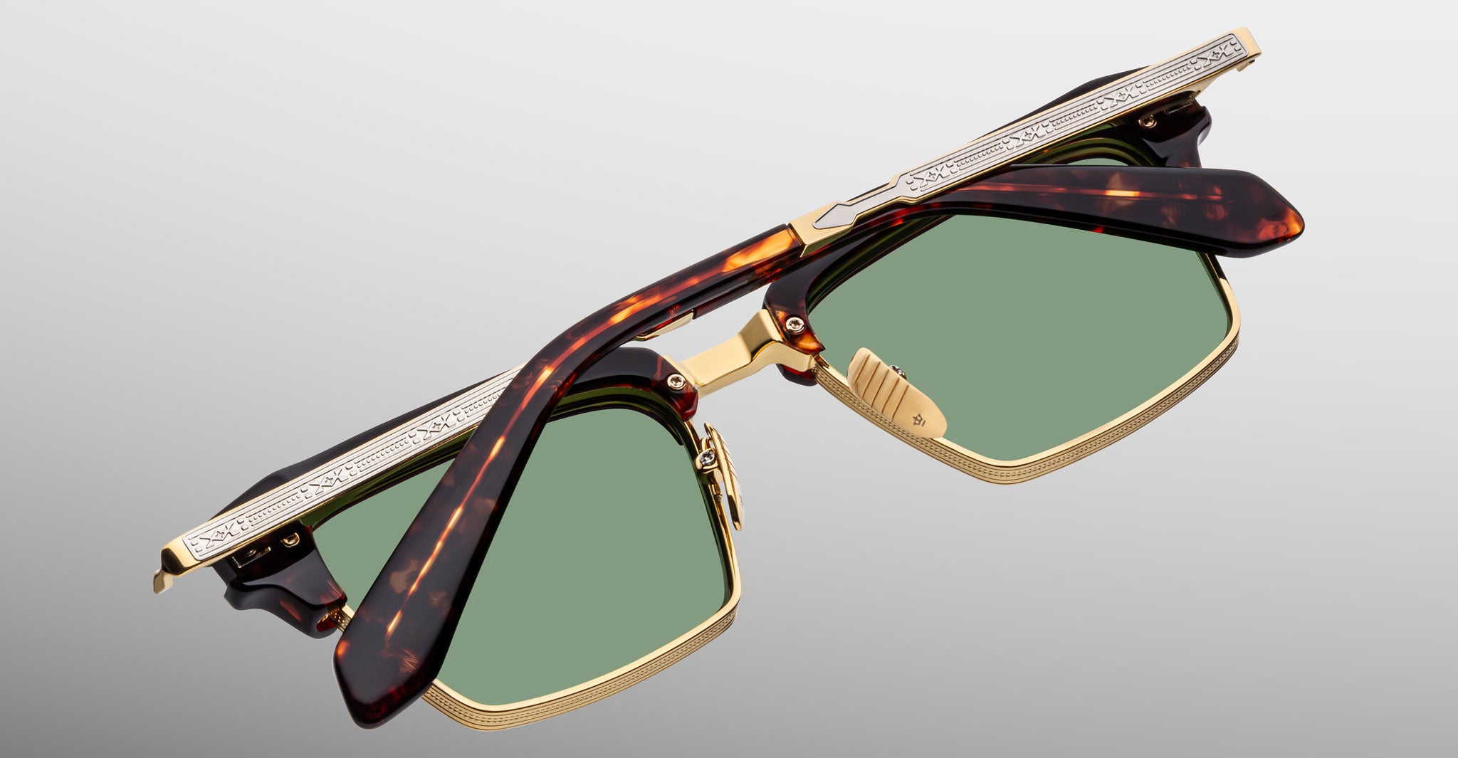 The Jacques Marie Mage Alin sunglasses, featuring a tortoiseshell and gold square frame with green lenses and engraved metal temples, are shown folded against a neutral gray background.