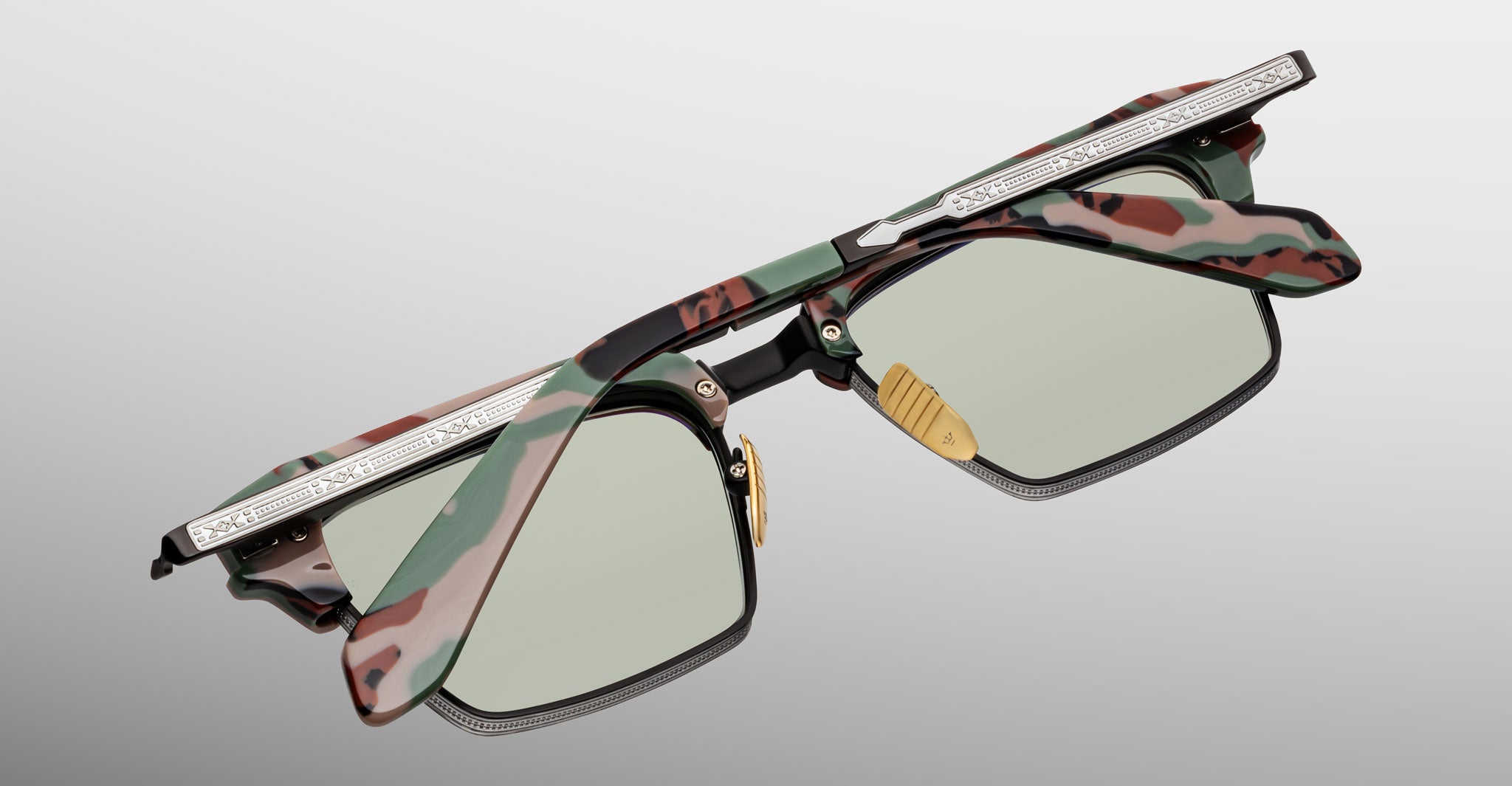 The Jacques Marie Mage Alin eyeglasses feature green-tinted lenses, a camouflage-patterned frame, and a silver metal accent on the top rim, shown against a light gray background.