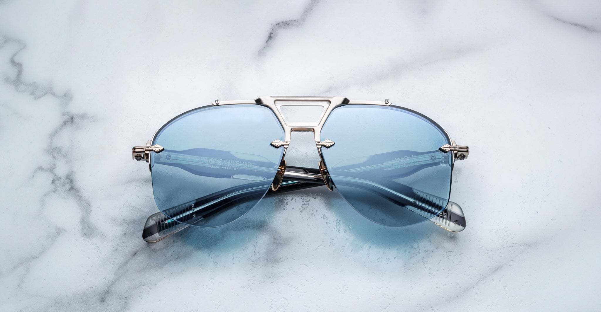 Jacques Marie Mage Alta aviator sunglasses with silver frames and blue-tinted lenses, viewed from above.