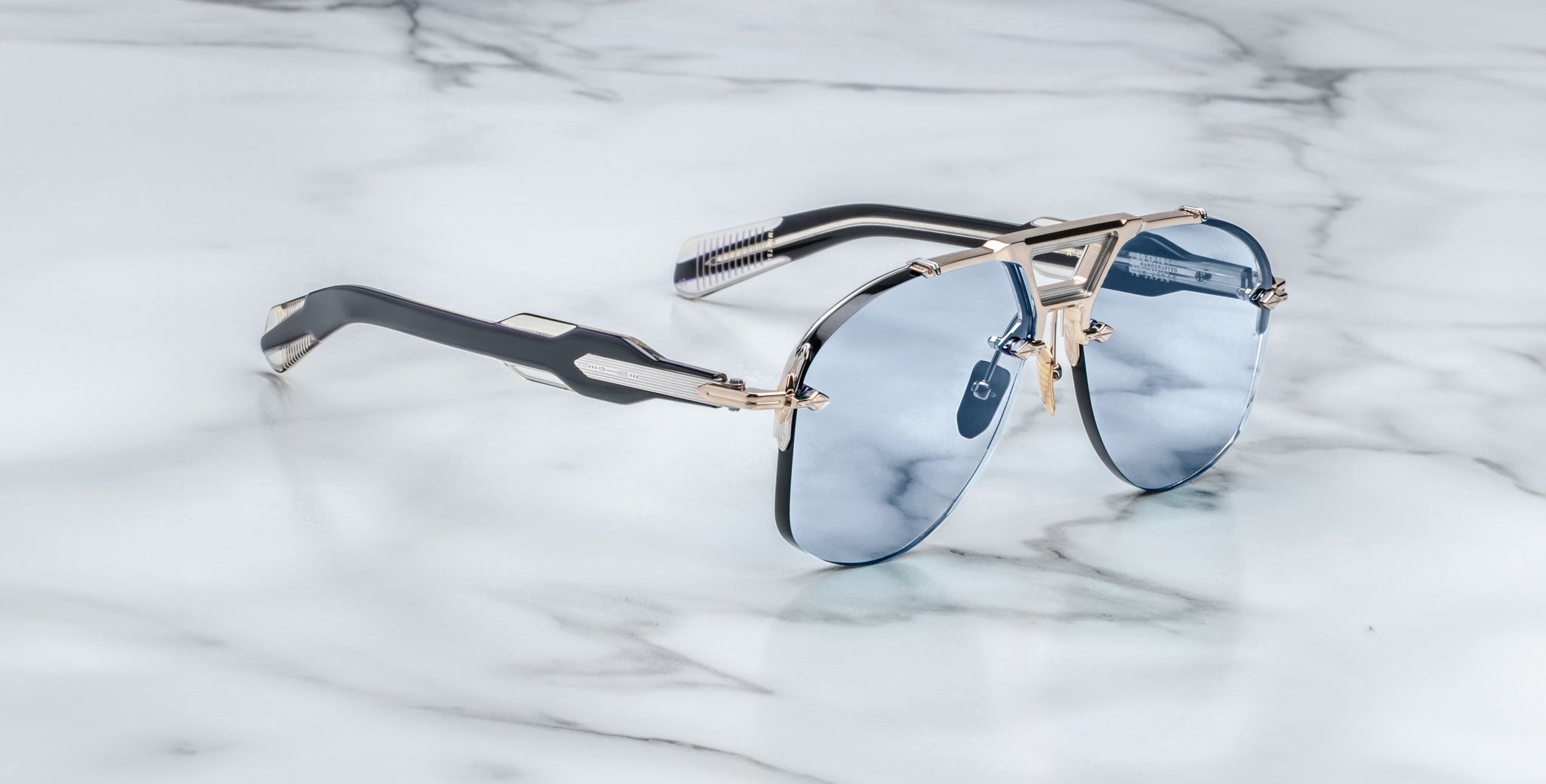 Jacques Marie Mage Alta sunglasses with blue lenses and metallic frames, top-down view.