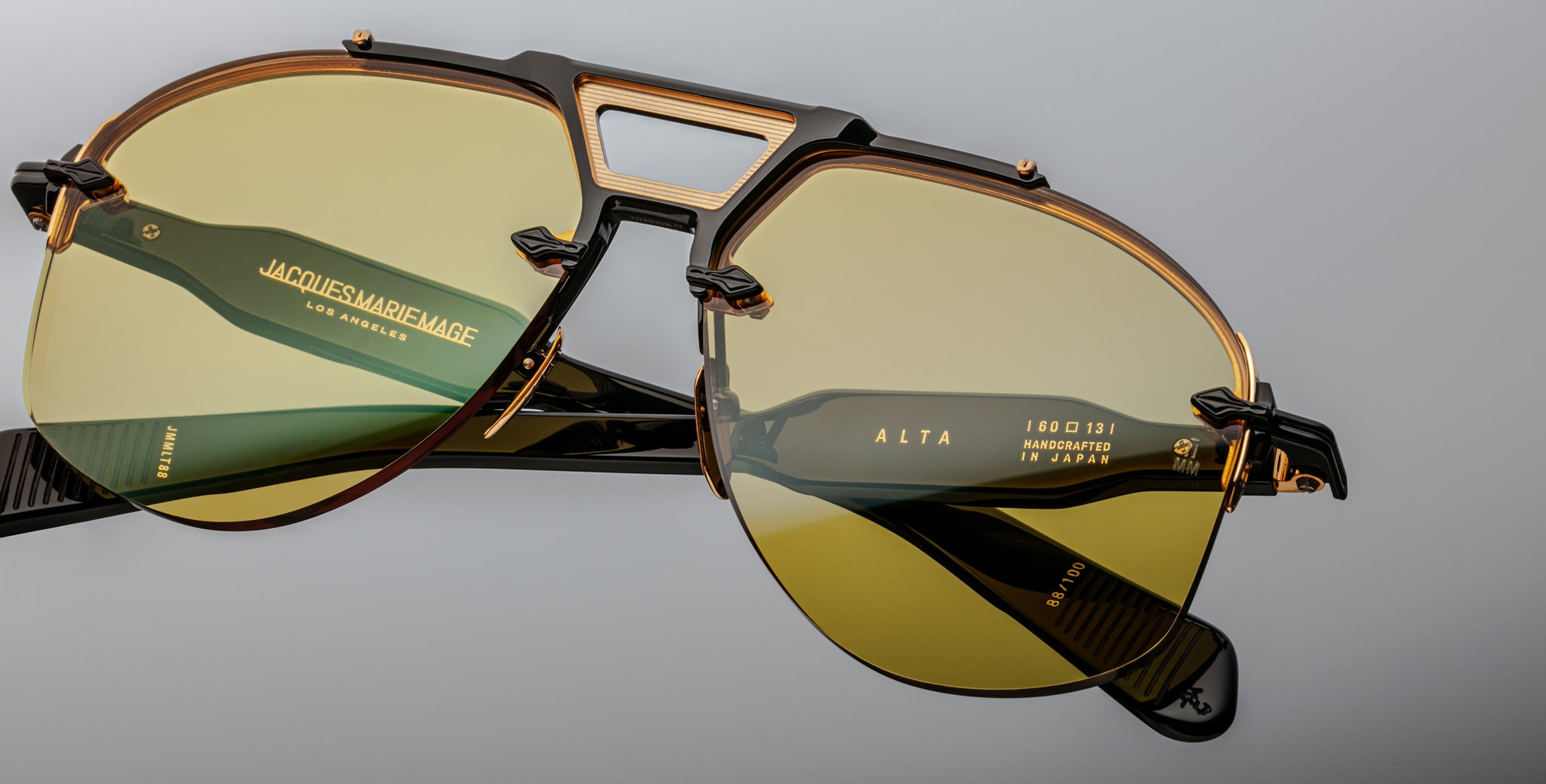 Close-up of Jacques Marie Mage Alta sunglasses in gold and black with yellow lenses and Handcrafted in Japan engraved.