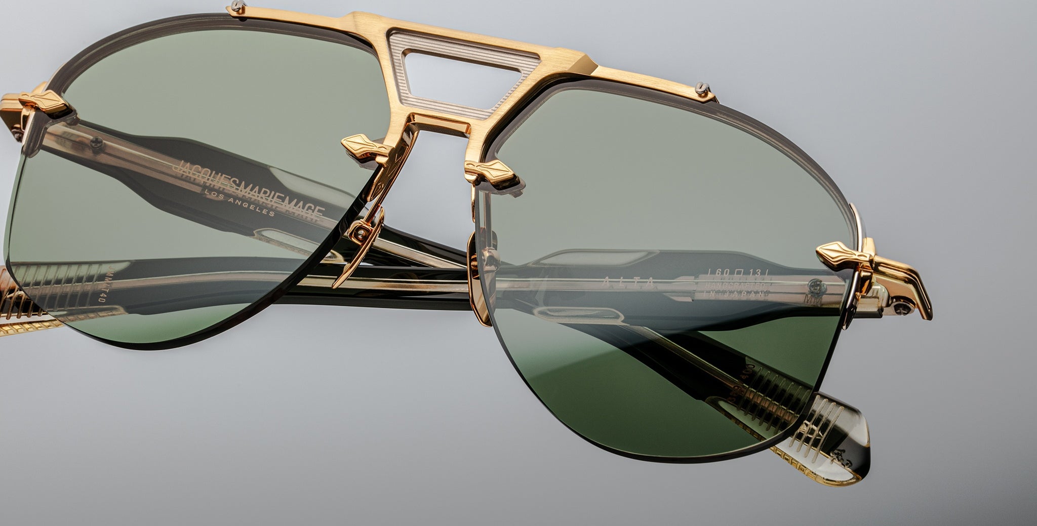 Close-up of Jacques Marie Mage Alta sunglasses, gold frames, green lenses, detailed arms visible from side angle.