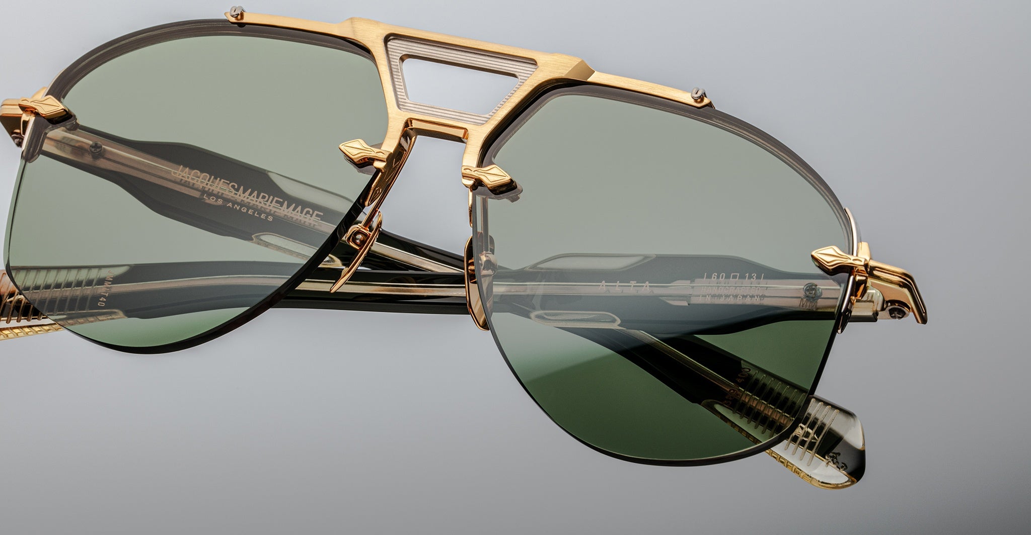 Close-up of Jacques Marie Mage Alta sunglasses, gold frames, green lenses, detailed arms visible from side angle.