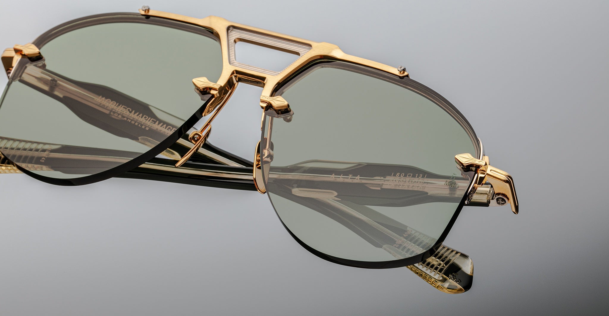 Jacques Marie Mage Alta sunglasses with gold frames and green lenses, shown from above.