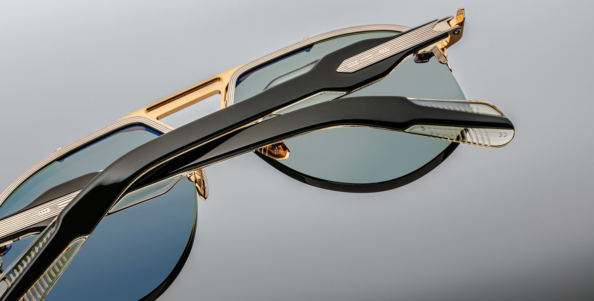 Close-up of two overlapping Jacques Marie Mage Alta sunglasses, gold frames, tinted lenses, front angle.