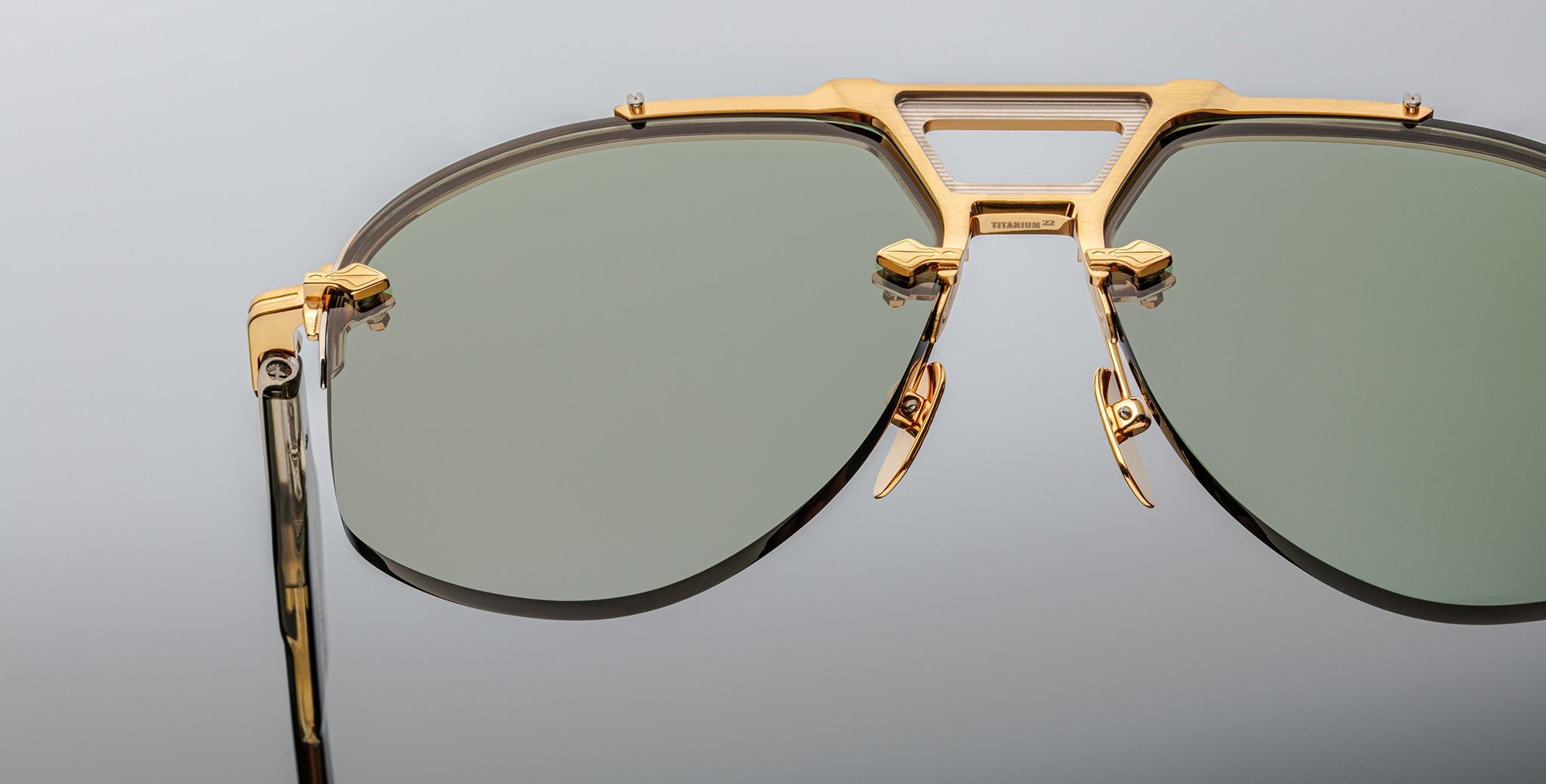 Close-up of Jacques Marie Mage Alta sunglasses, featuring gold frames and green lenses, viewed from the front.