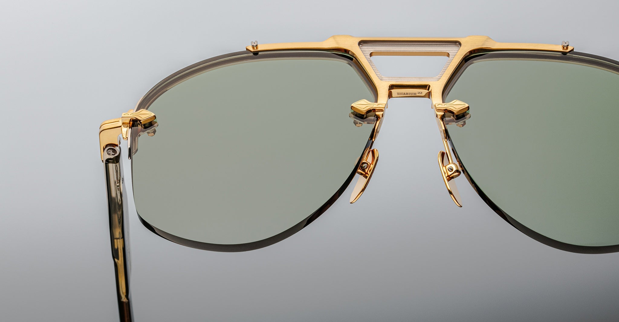 Close-up of Jacques Marie Mage Alta sunglasses, featuring gold frames and green lenses, viewed from the front.