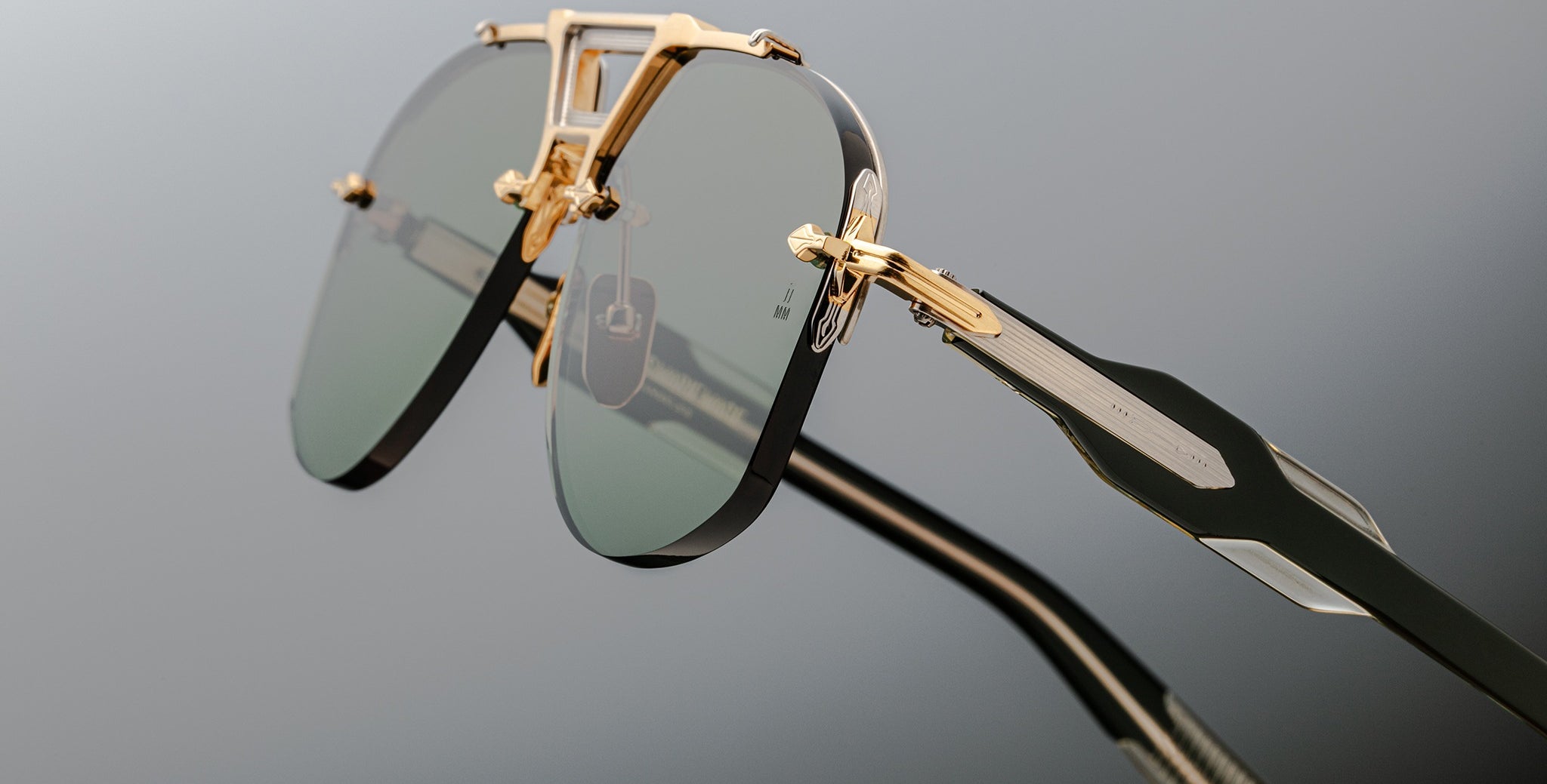Close-up of Jacques Marie Mage Alta sunglasses, featuring gold frames and green-tinted lenses, shown from the front angle.