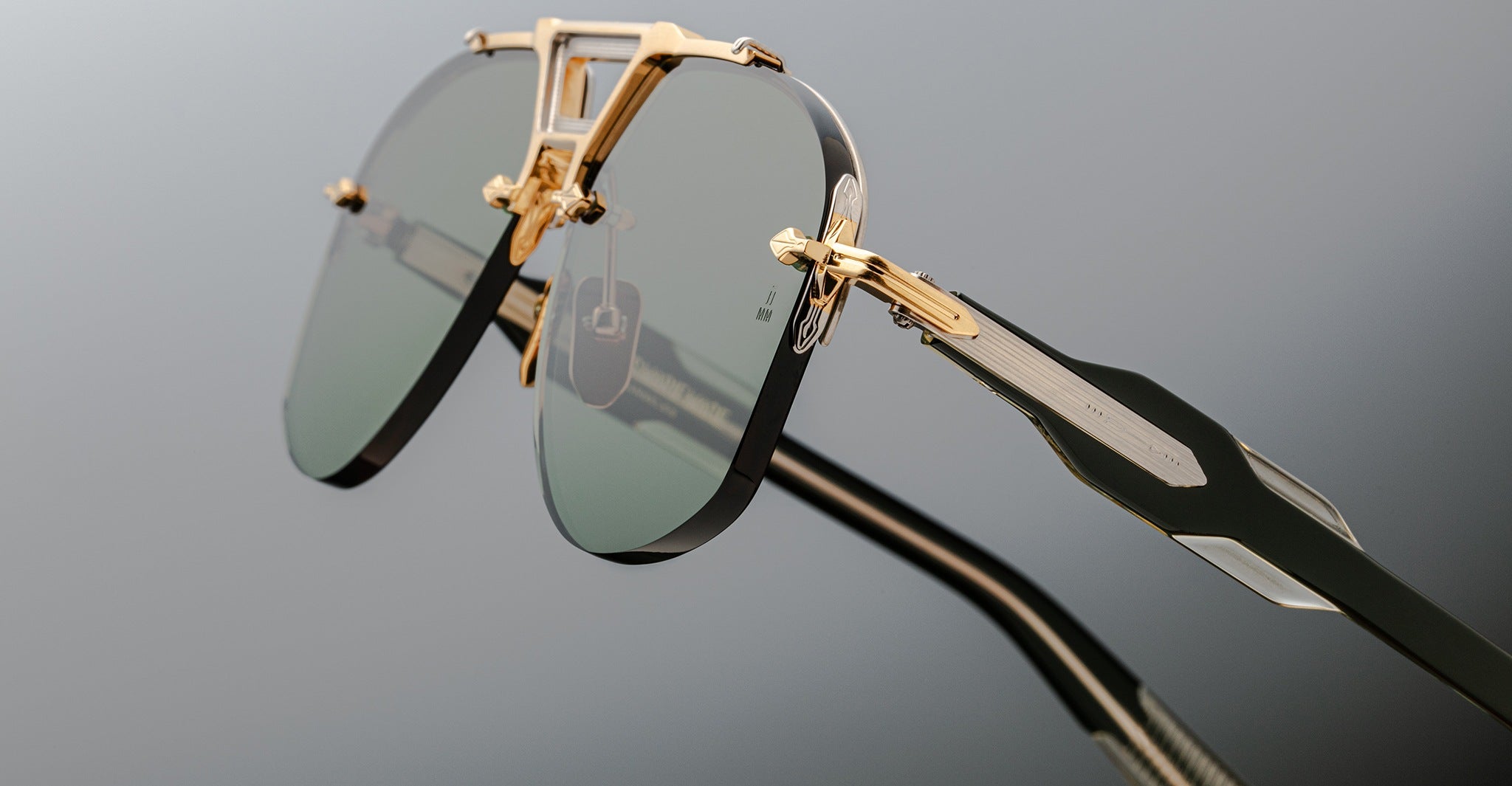 Close-up of Jacques Marie Mage Alta sunglasses, featuring gold frames and green-tinted lenses, shown from the front angle.