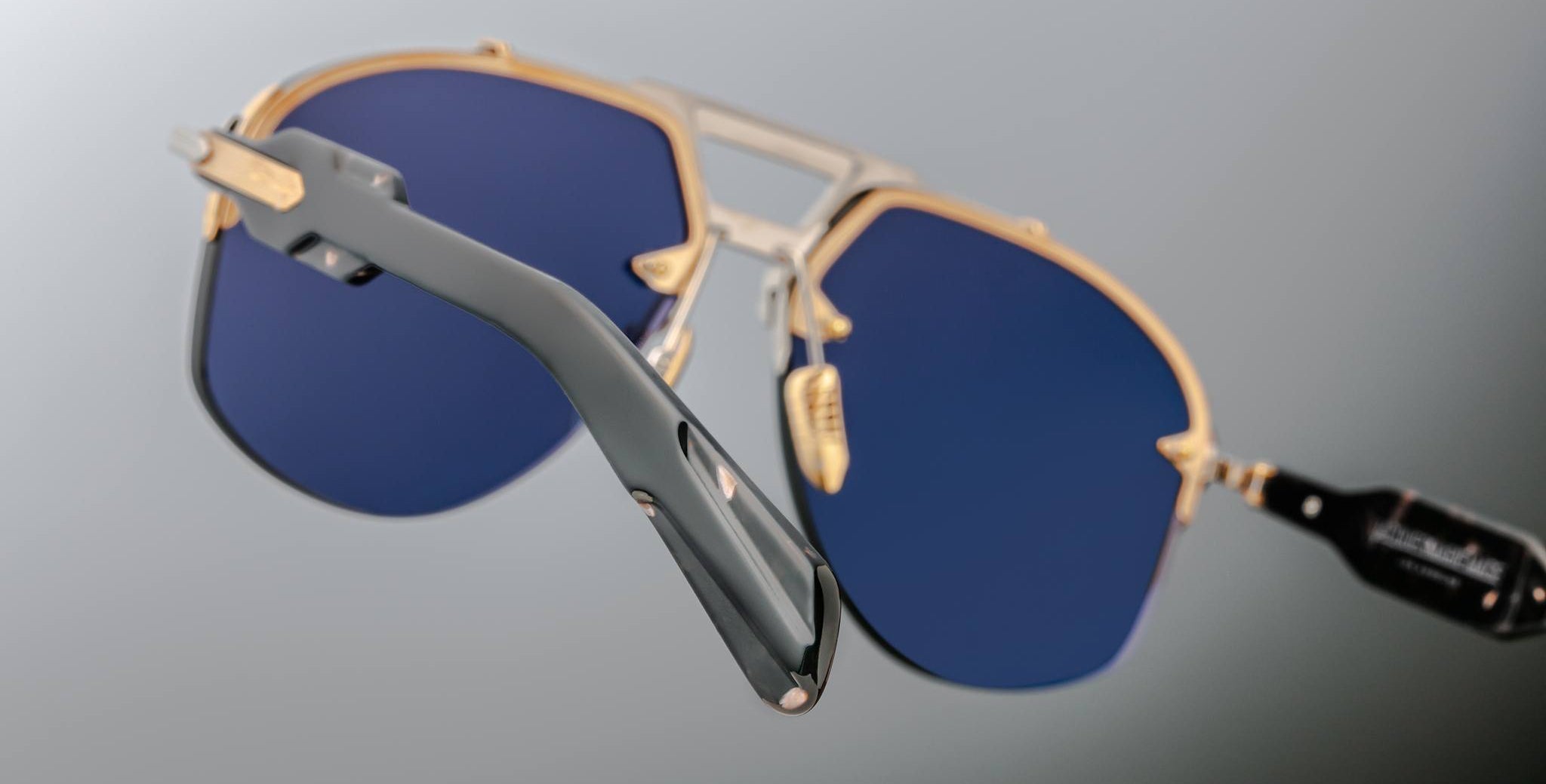 Close-up of Jacques Marie Mage Alta sunglasses, featuring blue lenses, gold accents, and dark arms, viewed from the front.