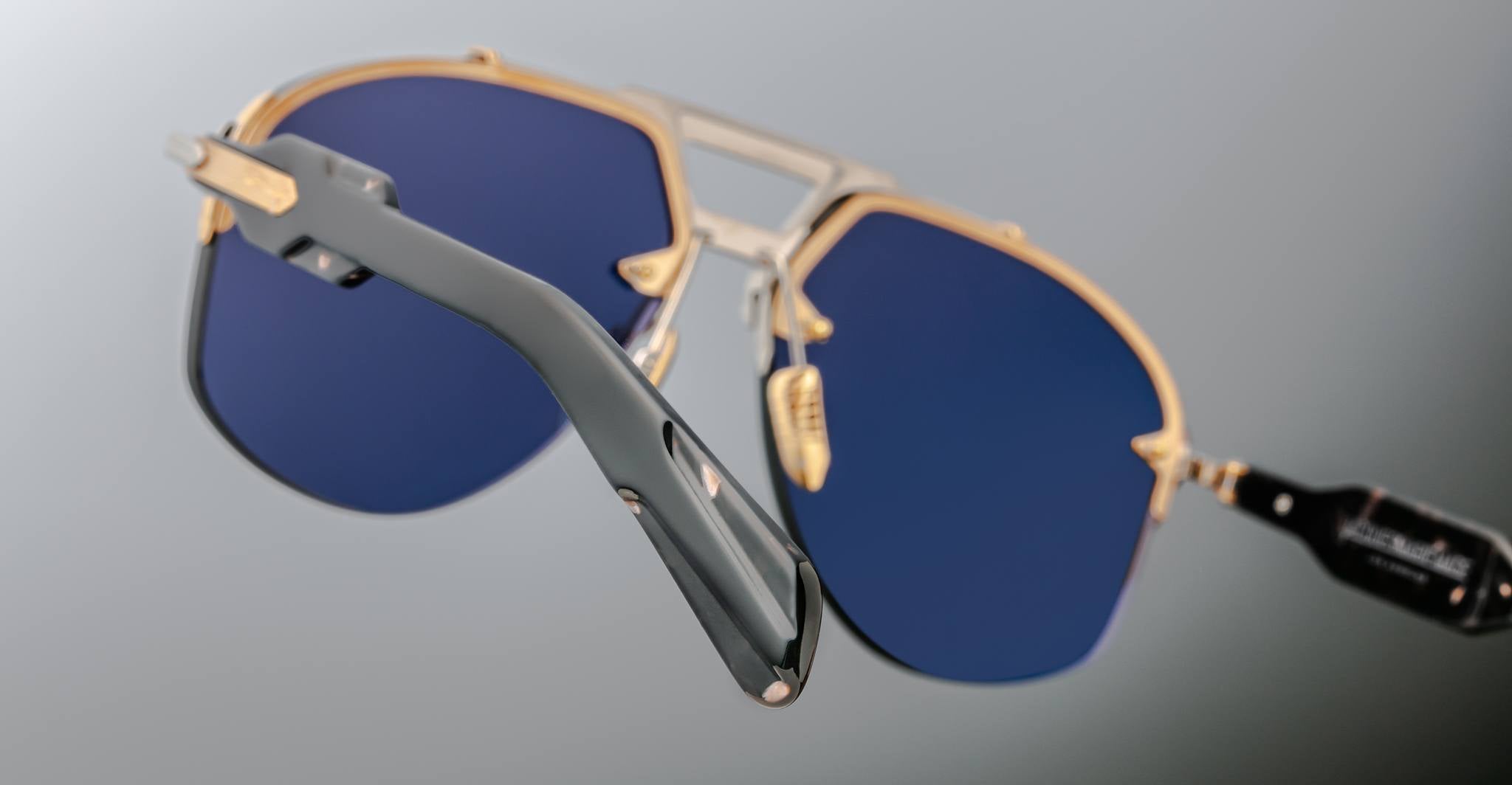 Close-up of Jacques Marie Mage Alta sunglasses, featuring blue lenses, gold accents, and dark arms, viewed from the front.