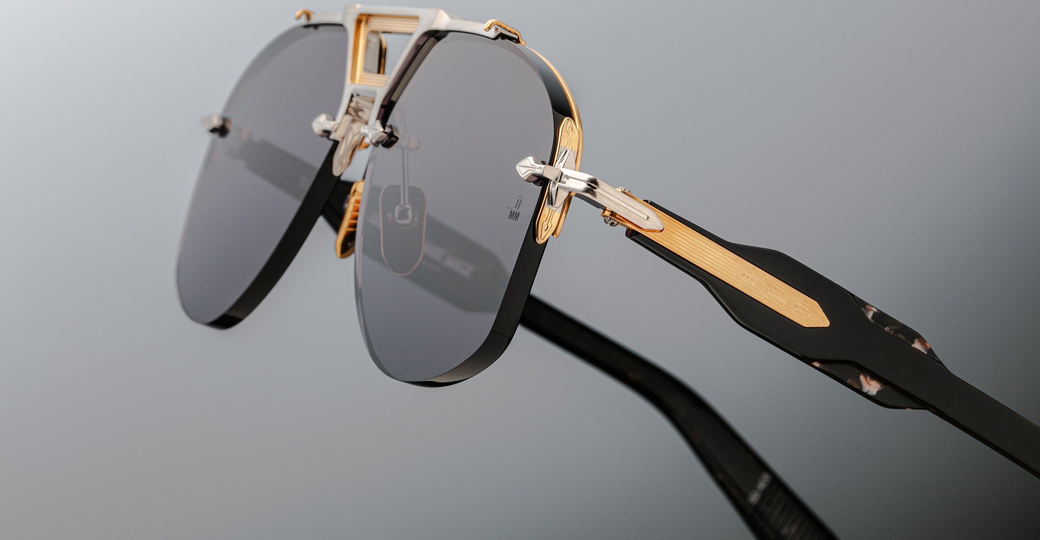 Close-up of Jacques Marie Mage Alta sunglasses with black lenses, gold accents, and geometric temples, front angle view.