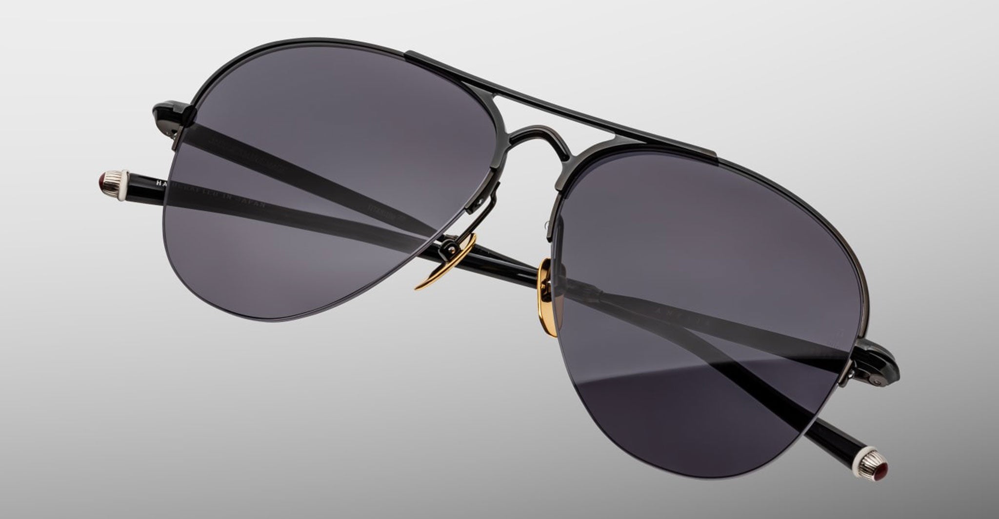 The Jacques Marie Mage Amelia sunglasses feature aviator-style black metal frames, thin arms, and dark tinted lenses, displayed against a plain light gray background.