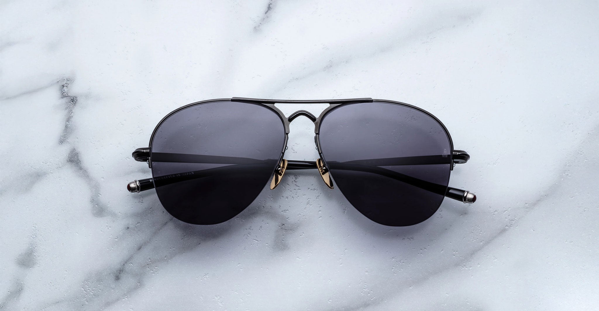 The Jacques Marie Mage Amelia sunglasses, featuring black aviator frames and dark lenses, rest on a white marble surface.