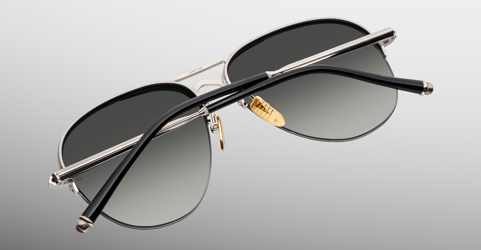 The Jacques Marie Mage Amelia sunglasses feature aviator-style silver metal frames, black gradient lenses, gold nose pads, and black temples, all displayed on a gray background.