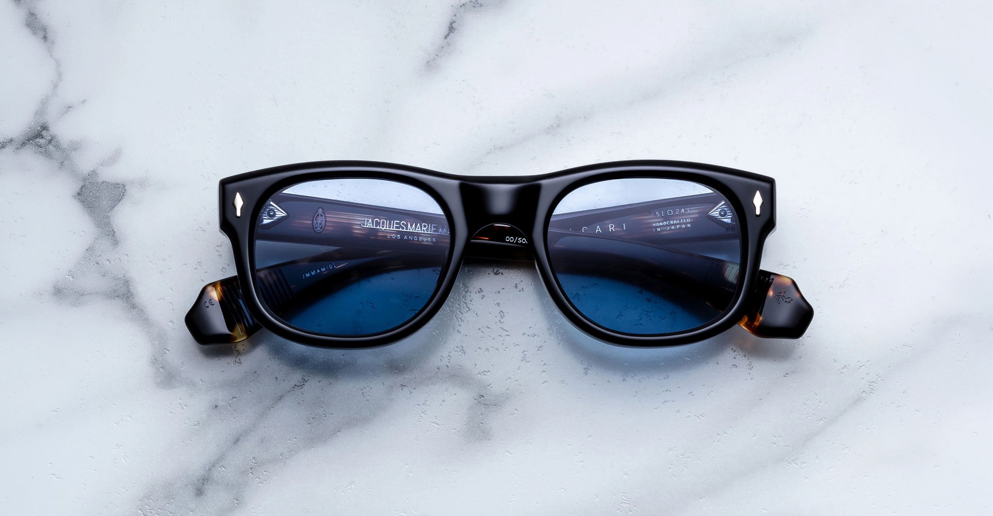 Jacques Marie Mage Amilcar sunglasses with black frames and blue lenses, top view.