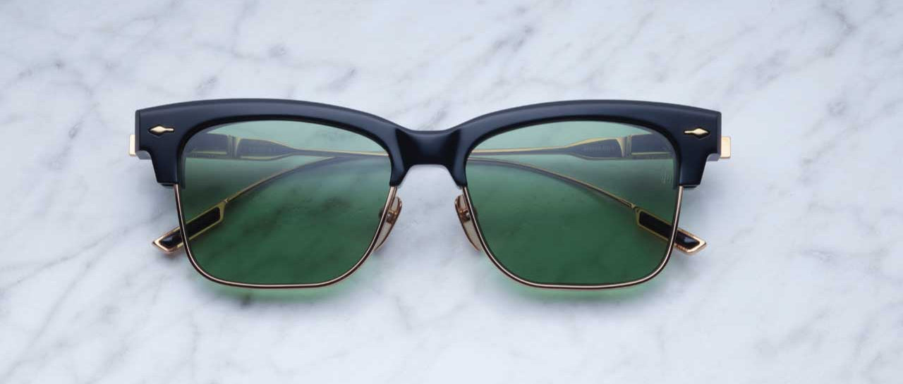 Jacques Marie Mage Apache sunglasses, black and gold frame with green lenses, viewed from above.
