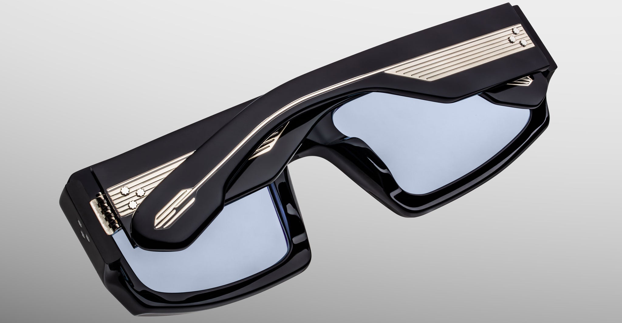 Top angled view of Jacques Marie Mage Apollo in Shadow highlighting the thick black acetate frame, beveled rectangular lenses with blue tint, sculpted temples with exposed engraved metal core, and signature arrowhead details.