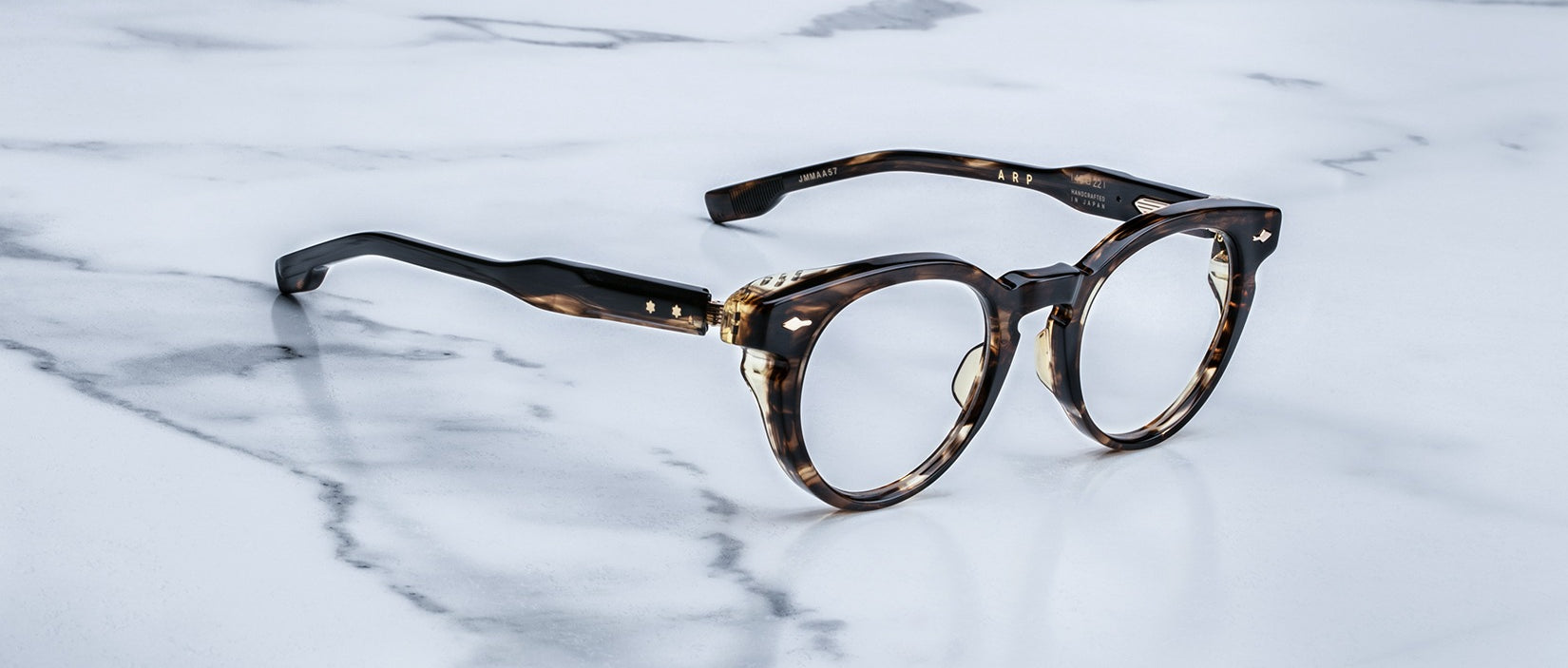 A pair of tortoiseshell round eyeglasses with gold accents rests on a white marble surface with gray veining.