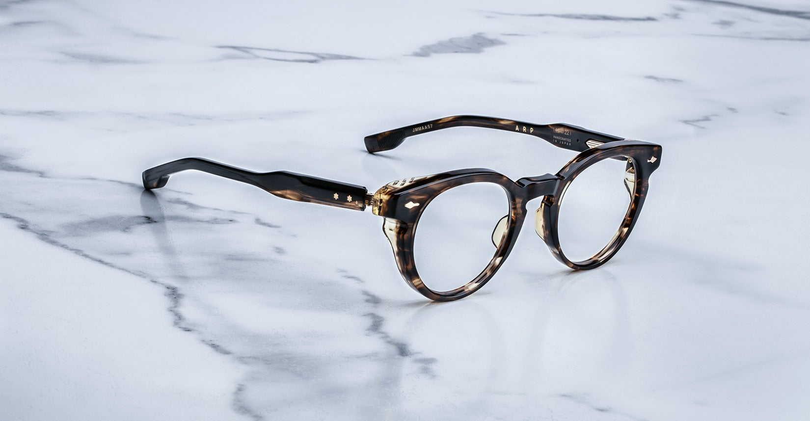 A pair of tortoiseshell round eyeglasses with gold accents rests on a white marble surface with gray veining.