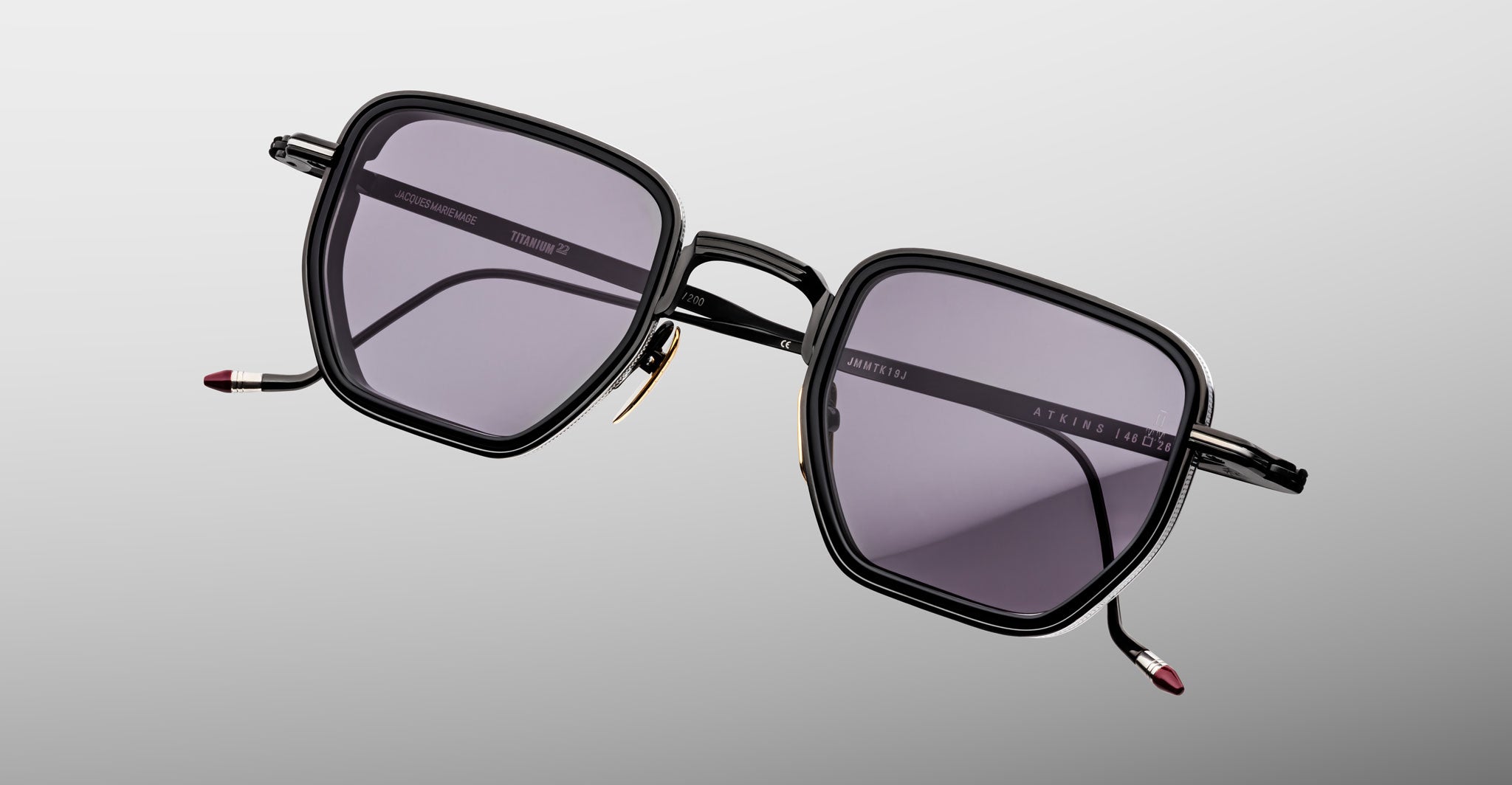 The Jacques Marie Mage Atkins are black, square-framed sunglasses with dark tinted lenses and slim metal arms, showcased on a light gray background—showing the essence of handcrafted Japanese eyewear.
