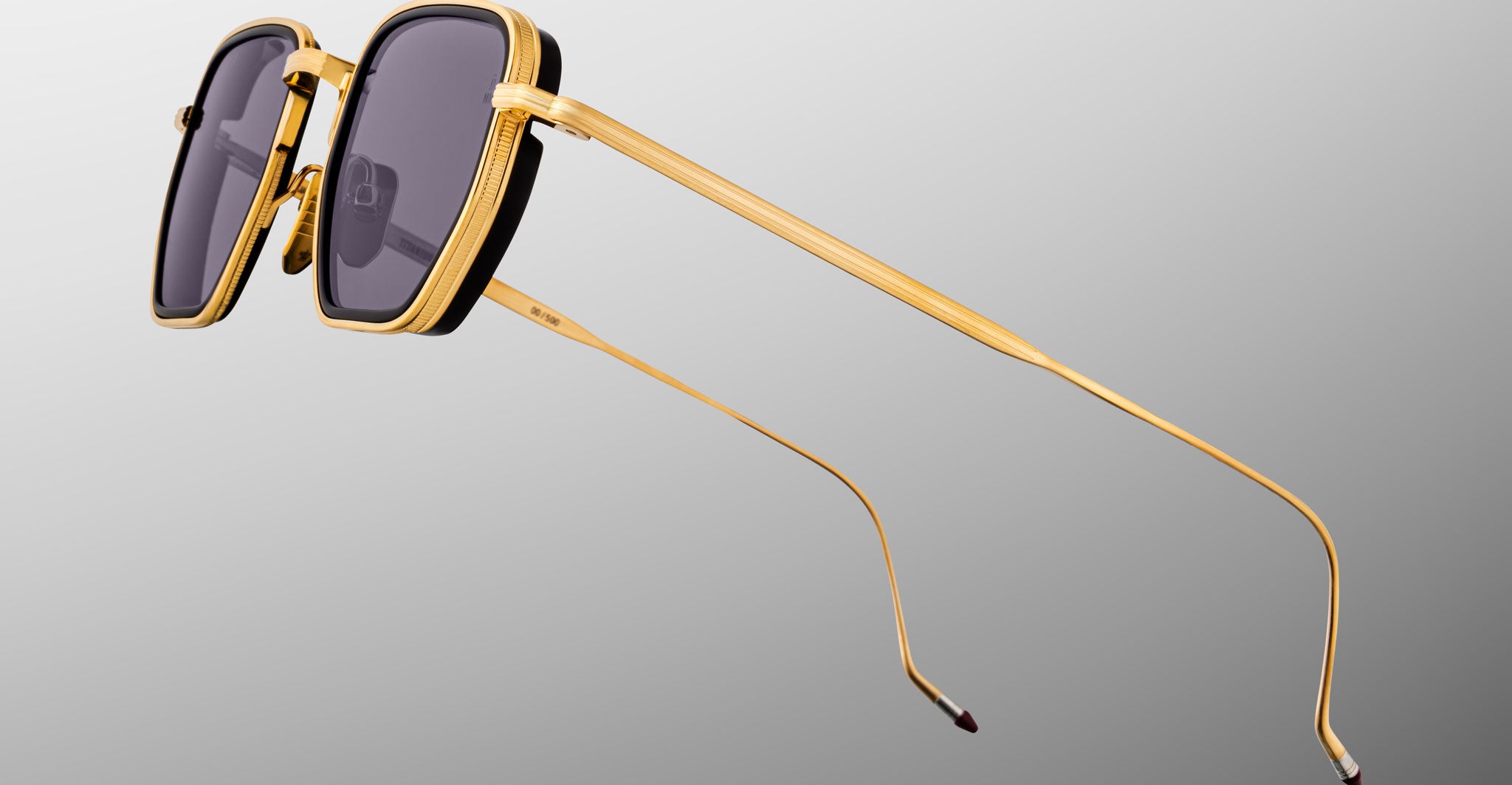 Close-up of Jacques Marie Mage Atkins sunglasses with gold rims, dark lenses, and thin temples viewed from the side.