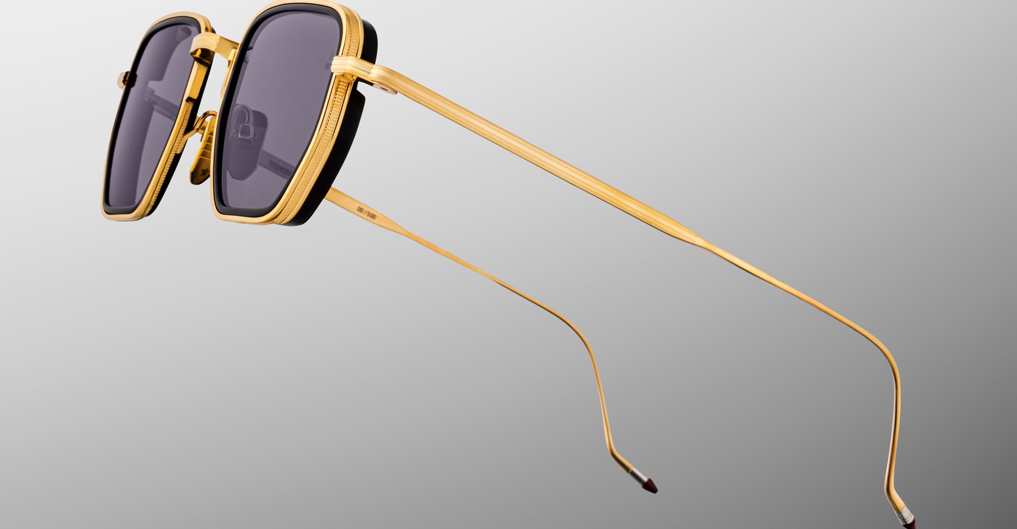 Close-up of Jacques Marie Mage Atkins sunglasses with gold rims, dark lenses, and thin temples viewed from the side.