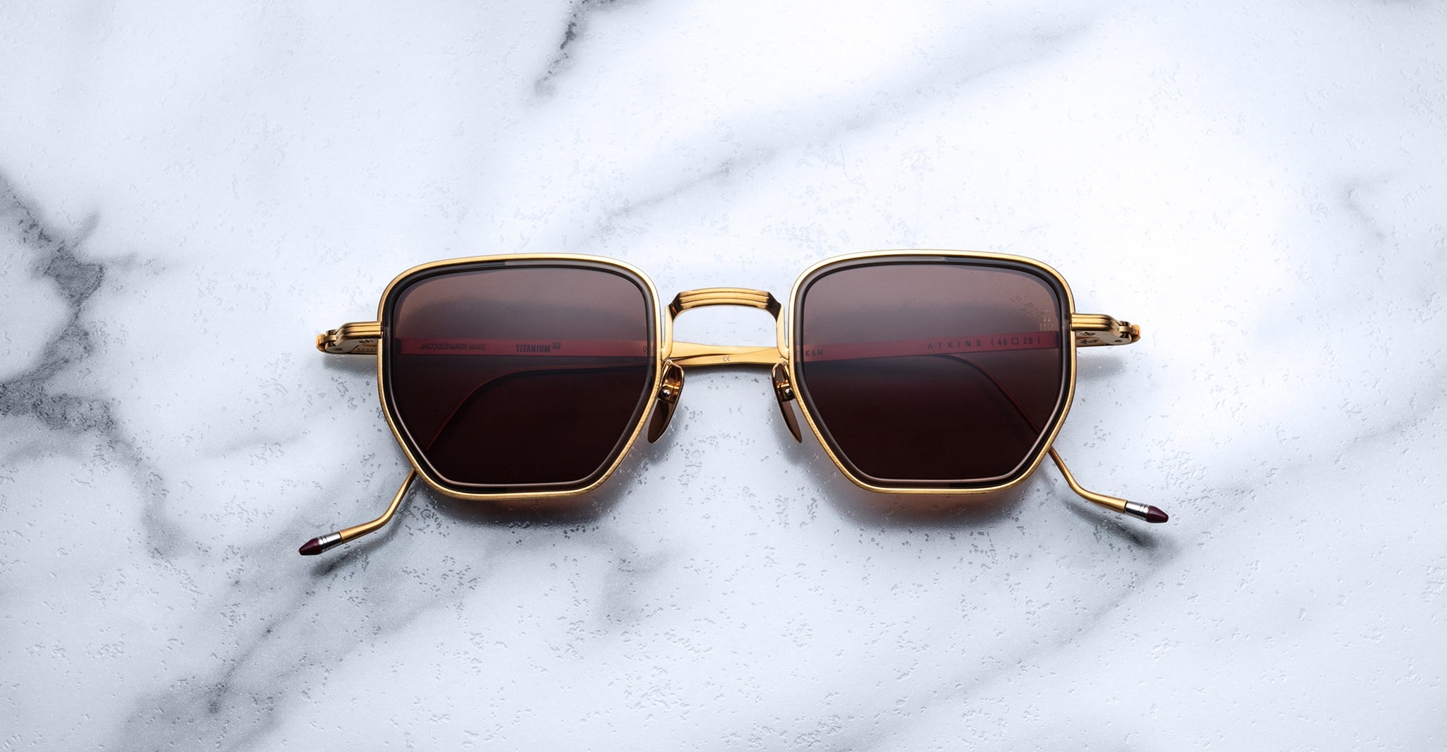 Jacques Marie Mage Atkins square sunglasses with gold frames and dark lenses, top view.