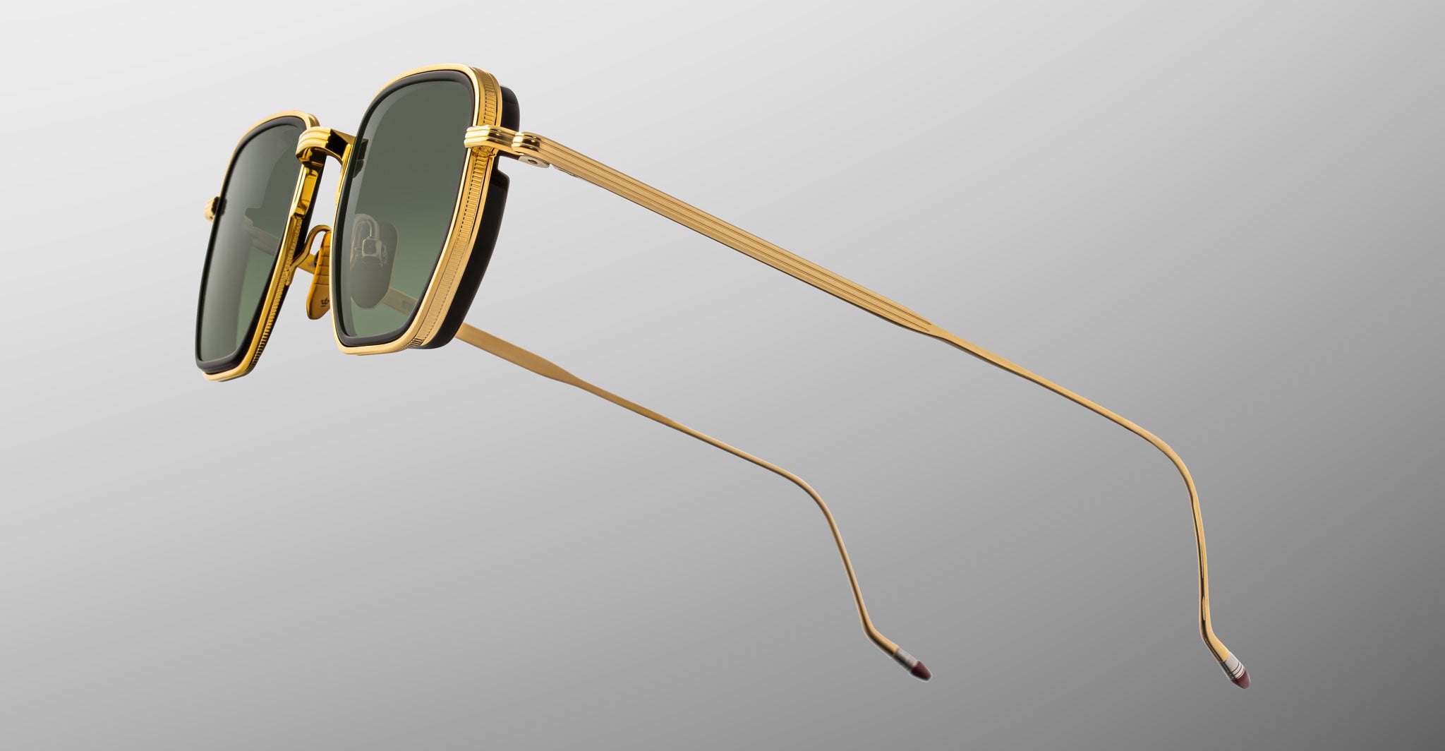 A pair of Jacques Marie Mage Atkins sunglasses with gold metal frames and dark green rectangular lenses, shown from a side angle on a light gray gradient background—showcasing exquisite handcrafted Japanese eyewear.
