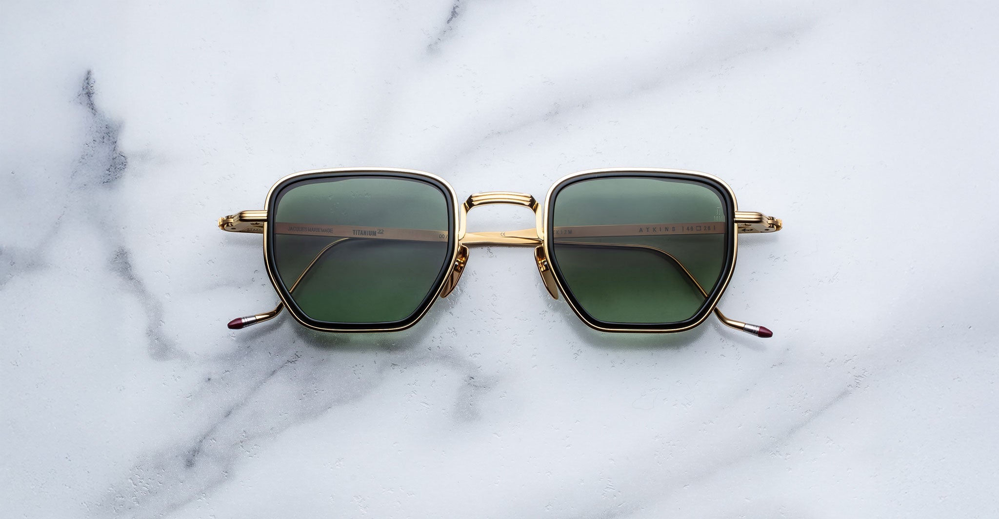 Jacques Marie Mage Atkins sunglasses featuring gold frames and green lenses, shown from above.