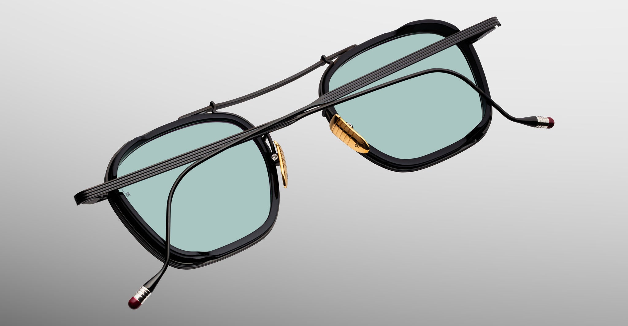 Jacques Marie Mage Baudelaire 2 black eyeglasses with gold nose pads and blue lenses, front view.