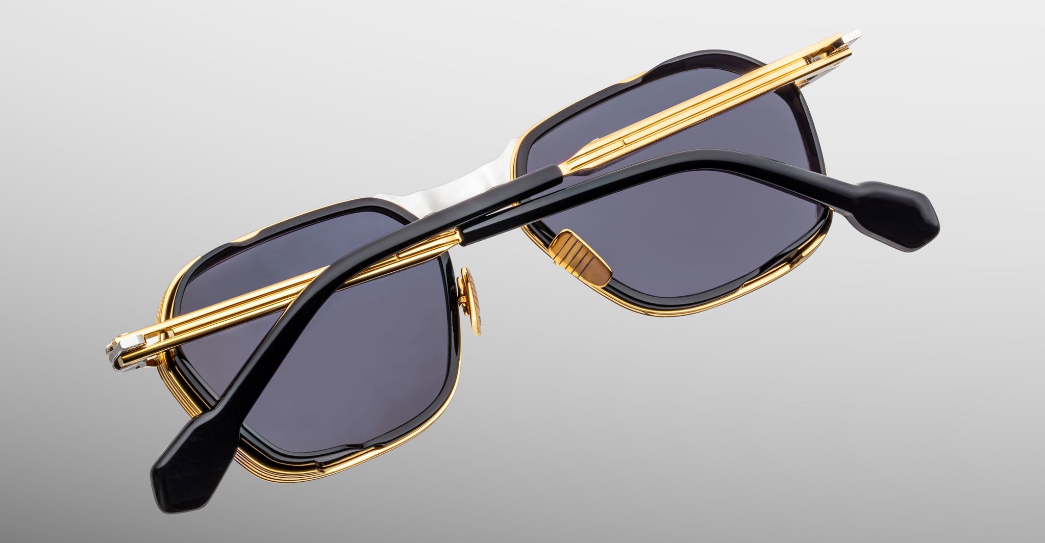 Jacques Marie Mage Beckett sunglasses feature gold and black limited-edition frames, dark rectangular lenses, and black temple arms, shown from the back against a light gray background.