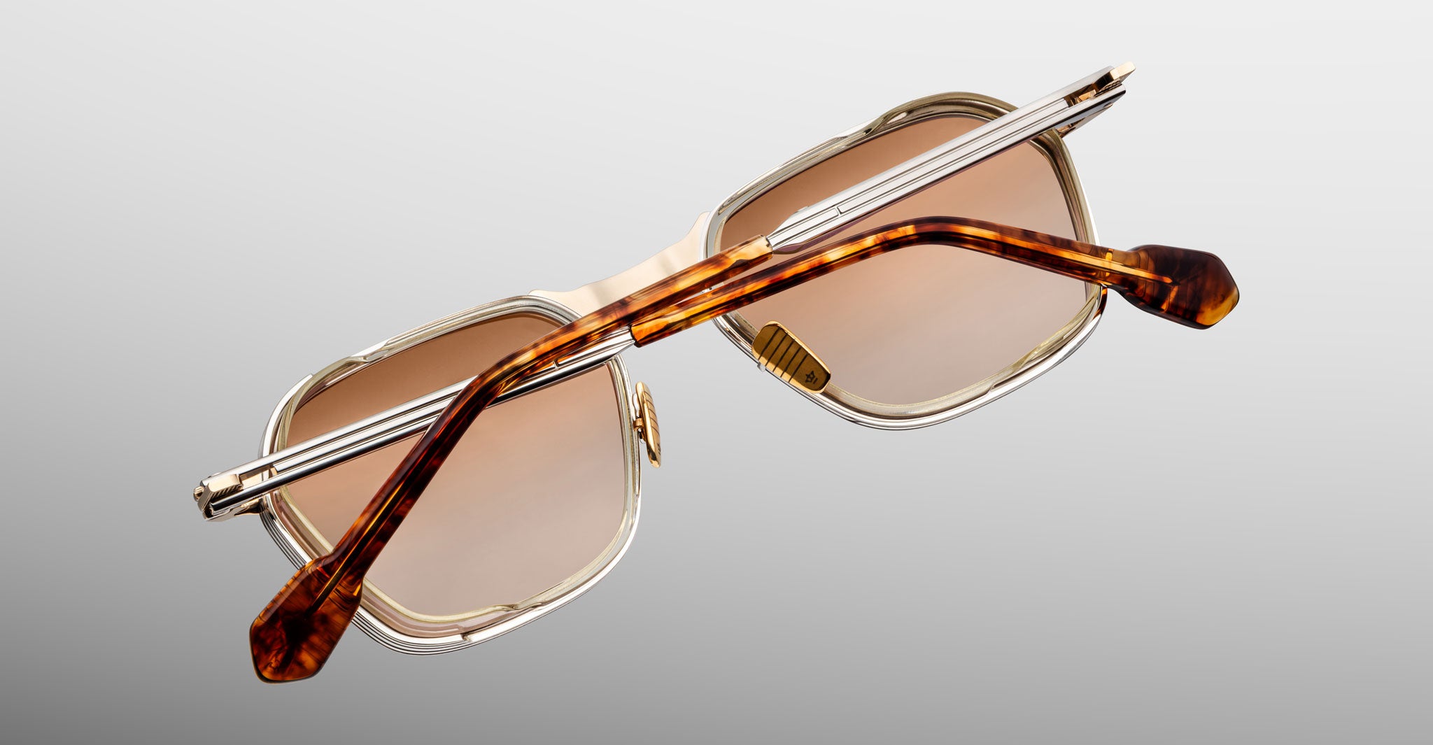 A pair of Jacques Marie Mage Beckett rectangular sunglasses with transparent rims, brown-tinted lenses, and brown tortoiseshell arms, handcrafted in Japan, shown from the back on a light gray background.
