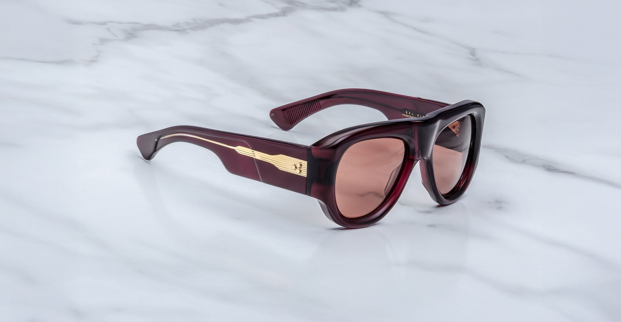 The Jacques Marie Mage Bel Air sunglasses, featuring oversized thick dark red translucent frames and brown tinted lenses, are displayed on a white marble surface.