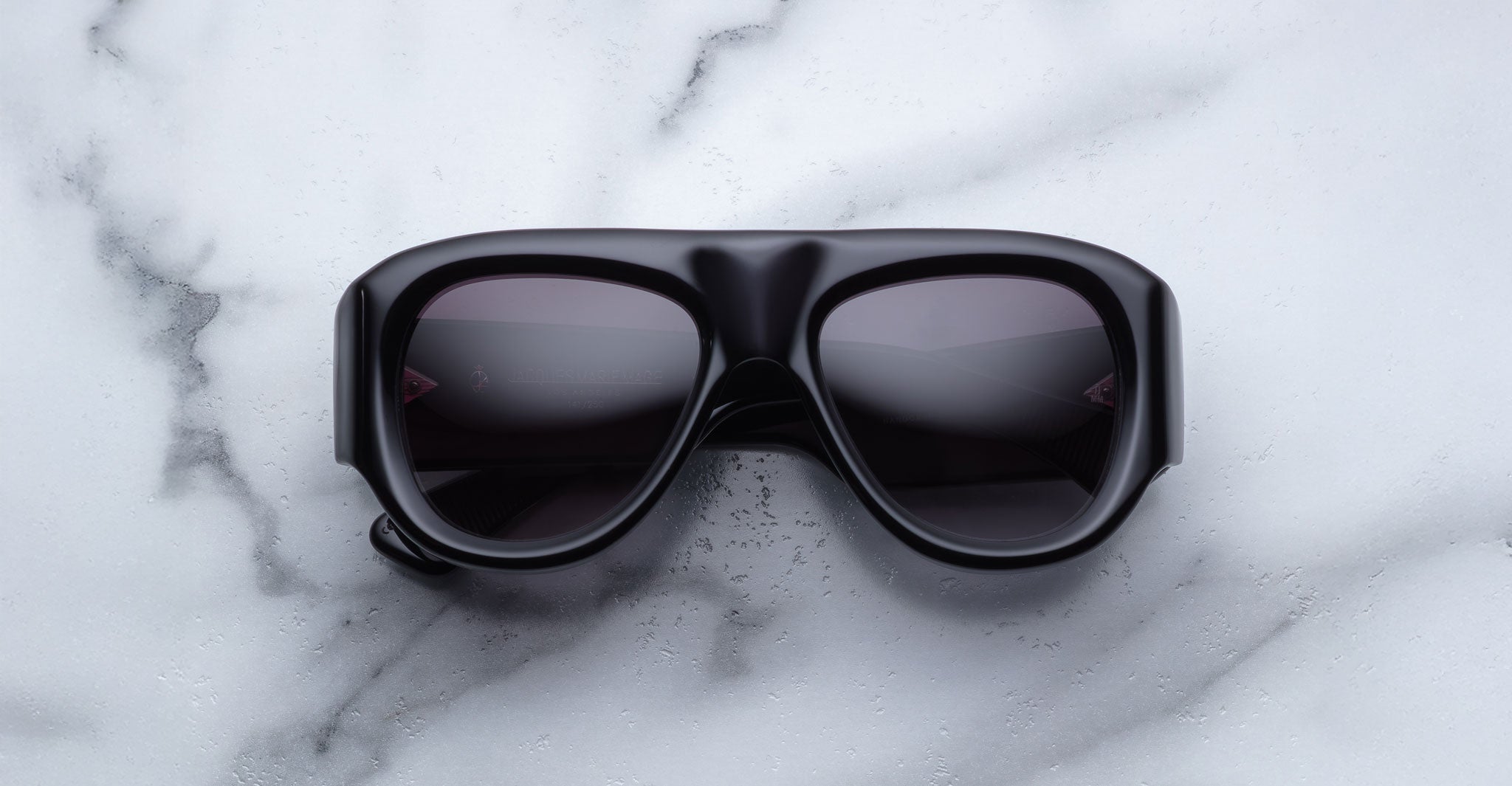 A pair of Jacques Marie Mage Bel Air oversized black sunglasses with thick frames and dark lenses, displayed on a white marble surface.