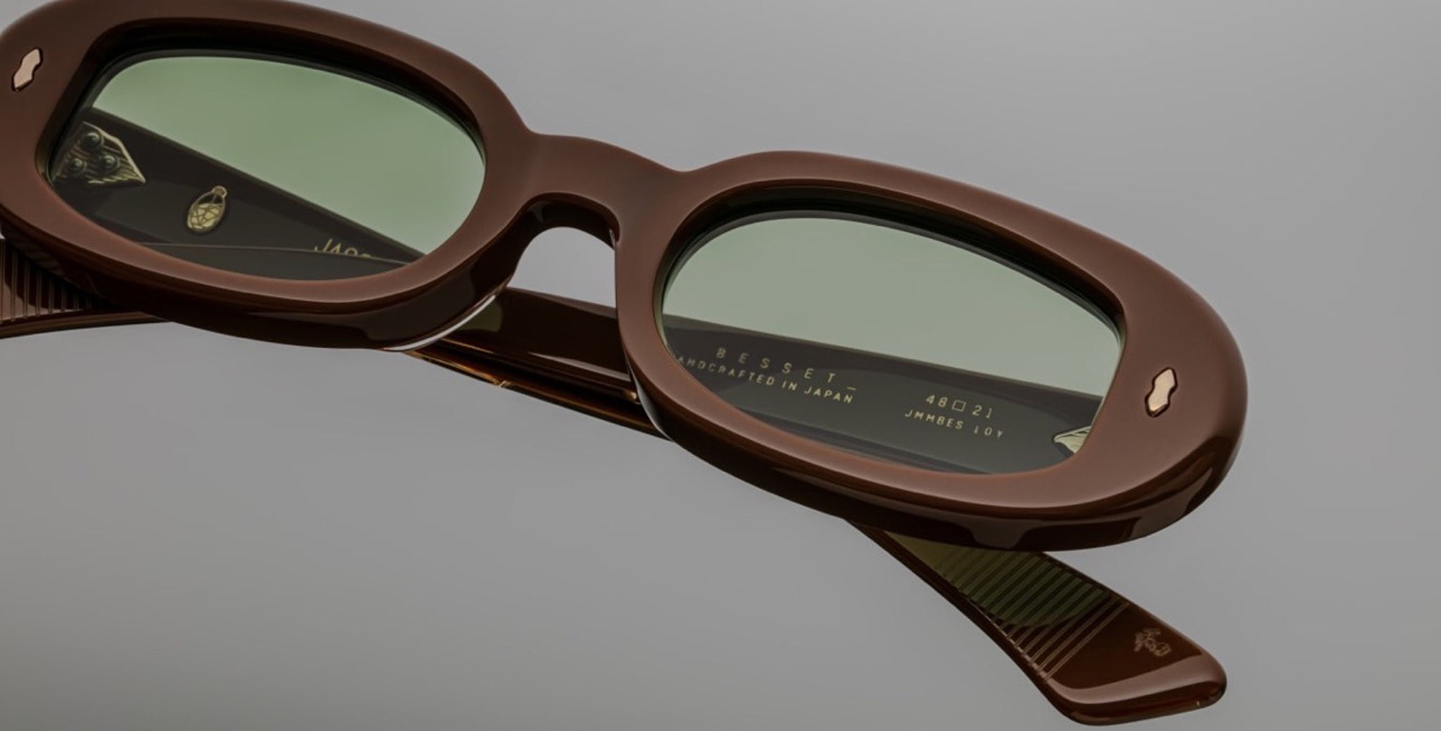 Close-up of Jacques Marie Mage Besset brown oval sunglasses with green lenses, front viewing angle.
