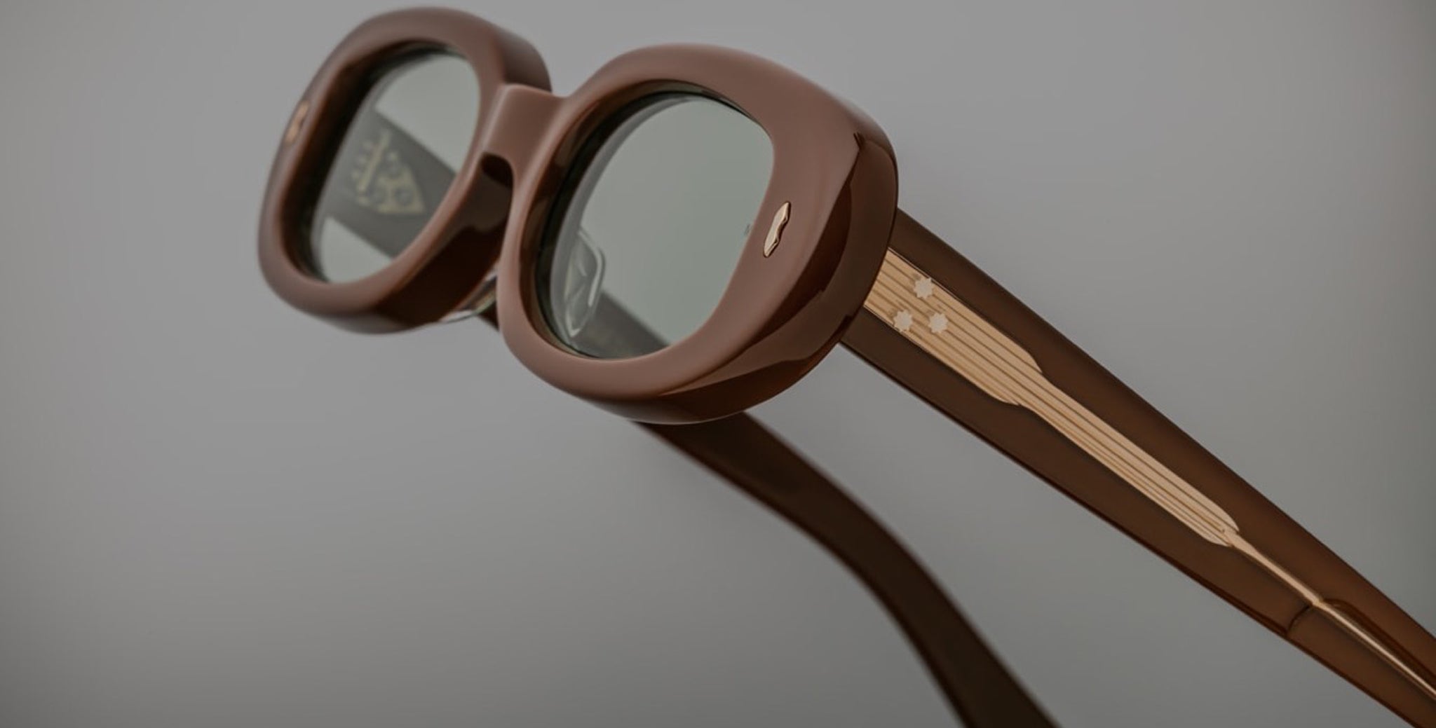 Close-up of Jacques Marie Mage Besset sunglasses, brown oval frames, tinted lenses, gold detailing, front angle.